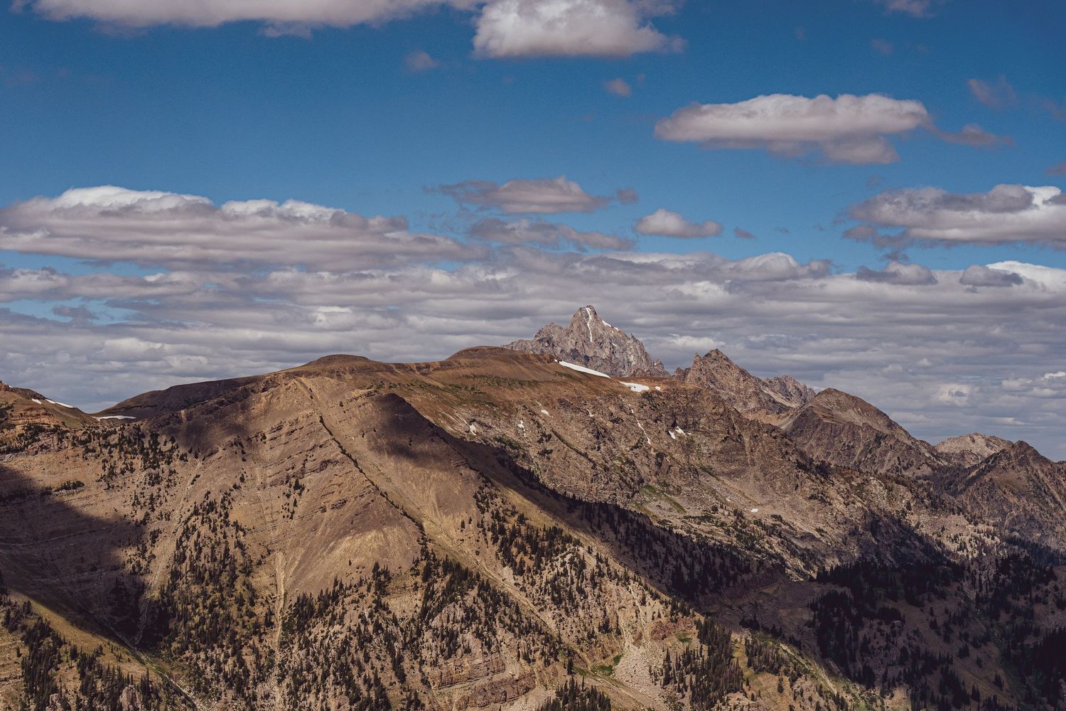 Panoramic view of rocky mountain ranges under blue sky with scattered white clouds.