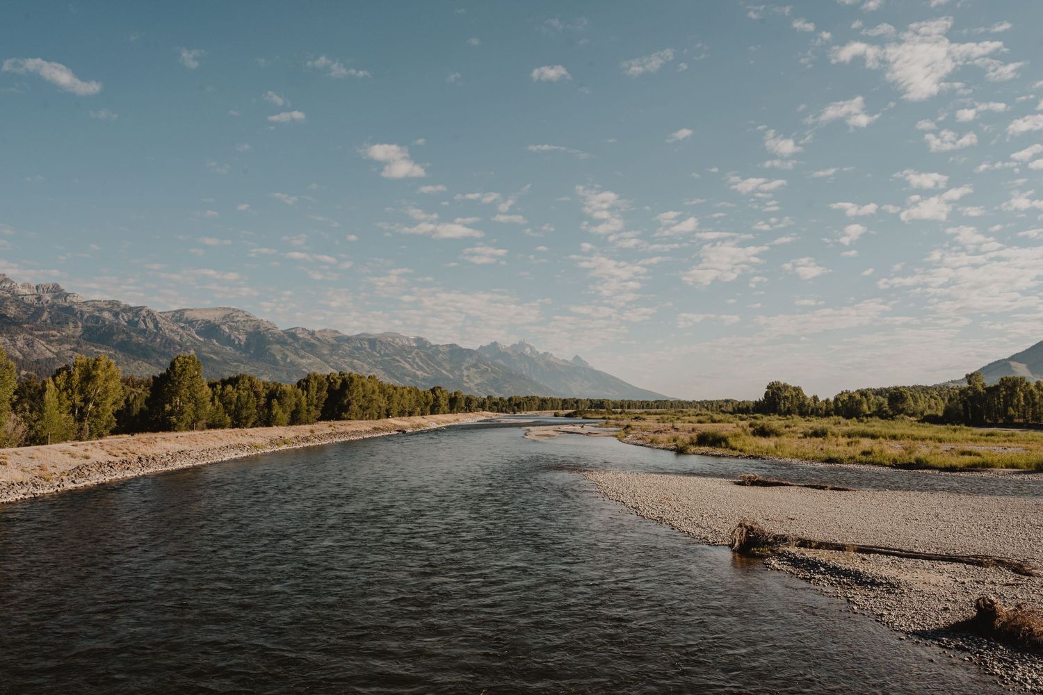 Scenic mountain landscape with winding river and autumn trees reflecting in calm waters under blue sky.