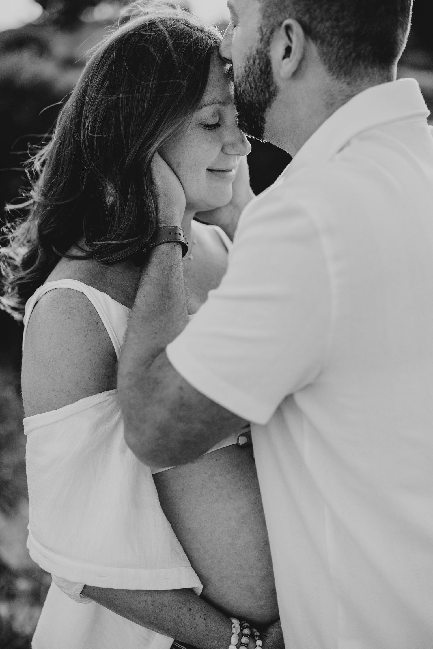 Intimate black and white photo of a couple sharing a tender moment outdoors.