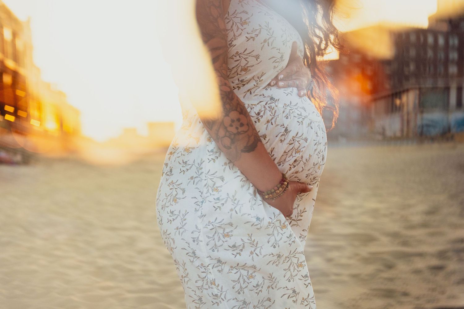 Side profile of a pregnant woman in lace dress on beach during golden hour.