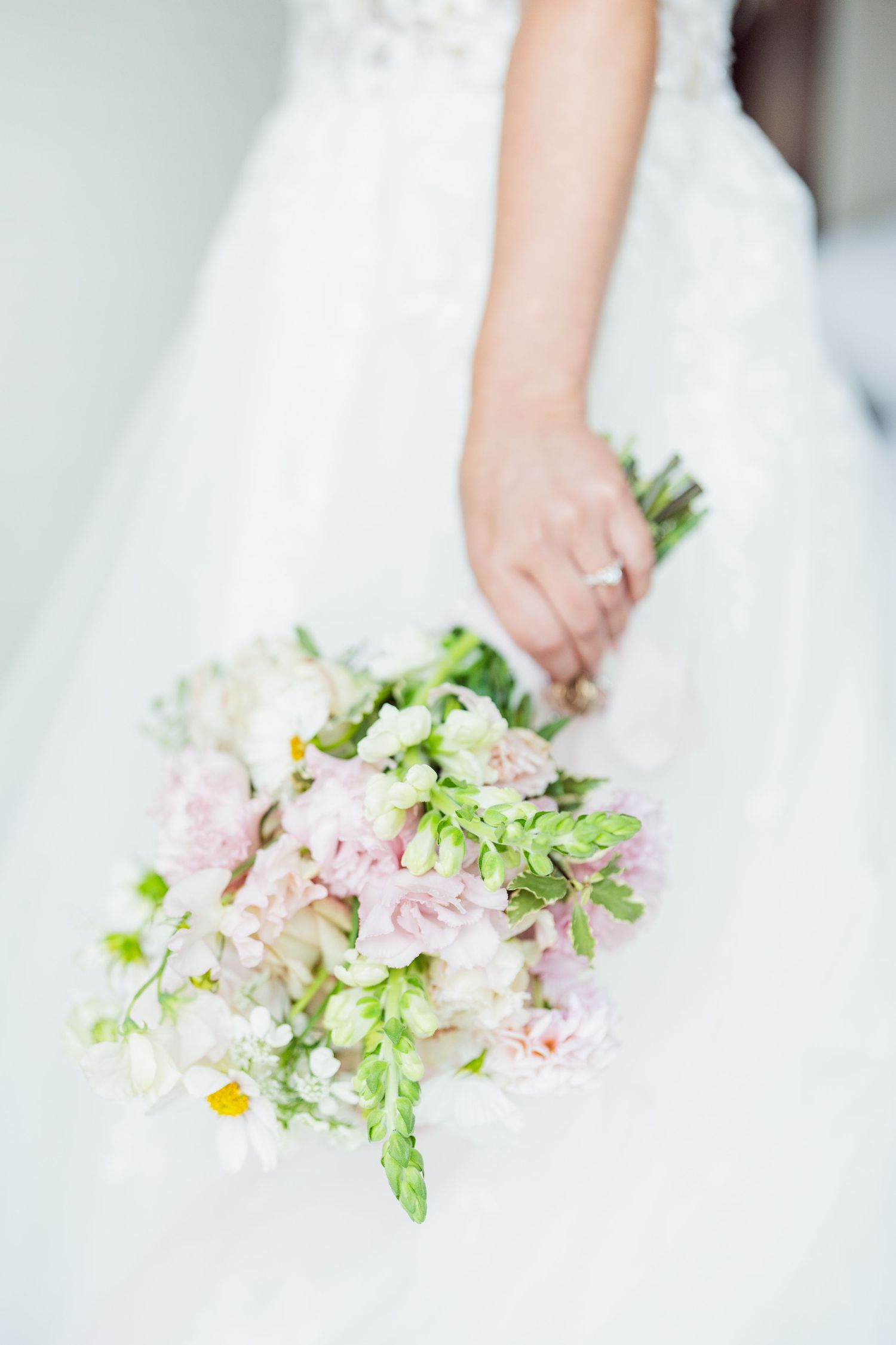 Soft focus image of hands holding delicate pink and green floral wedding bouquet.