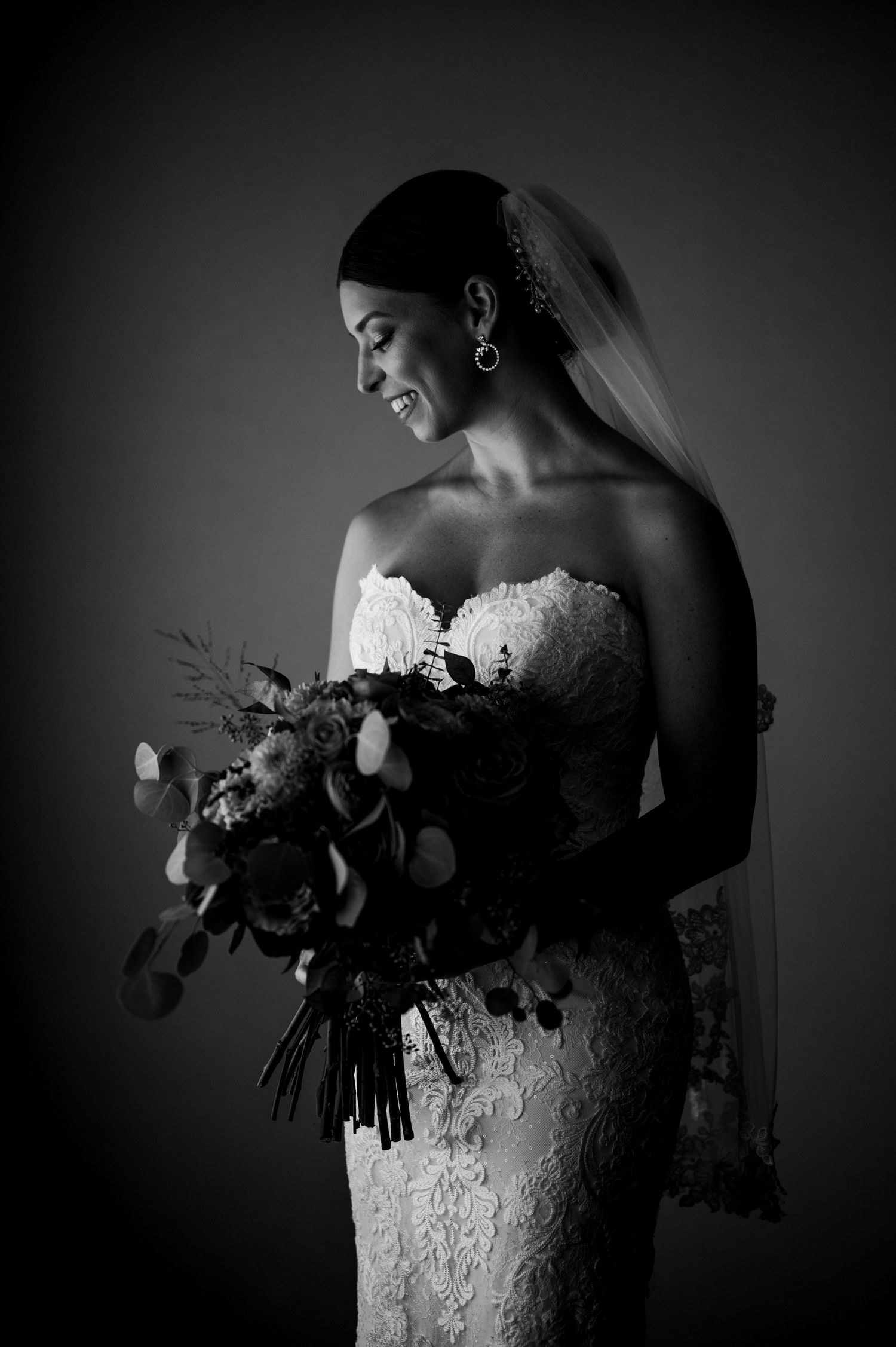Dramatic black and white photos of a bride holding a bouquet in lace wedding dress.