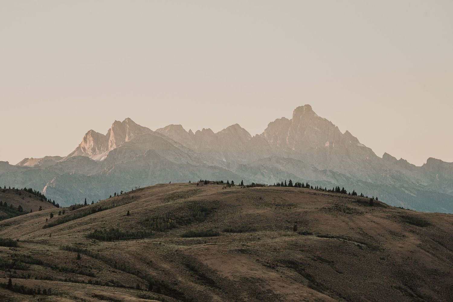 Dramatic mountain peaks silhouetted against a hazy sunset sky in Grand Teton National Park.