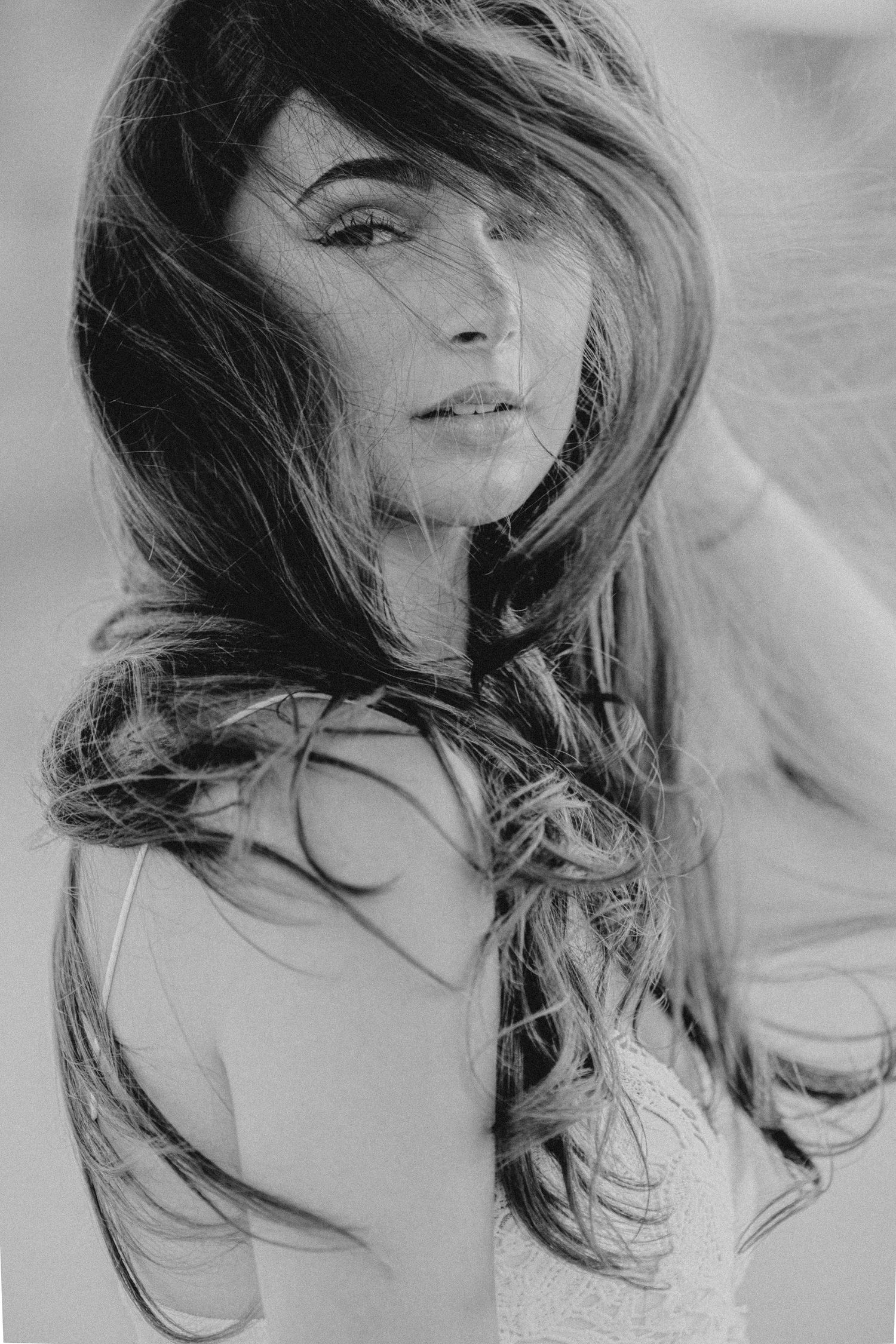 Black and white portrait of a woman with long flowing hair blowing in the wind, soft focus outdoor photography.