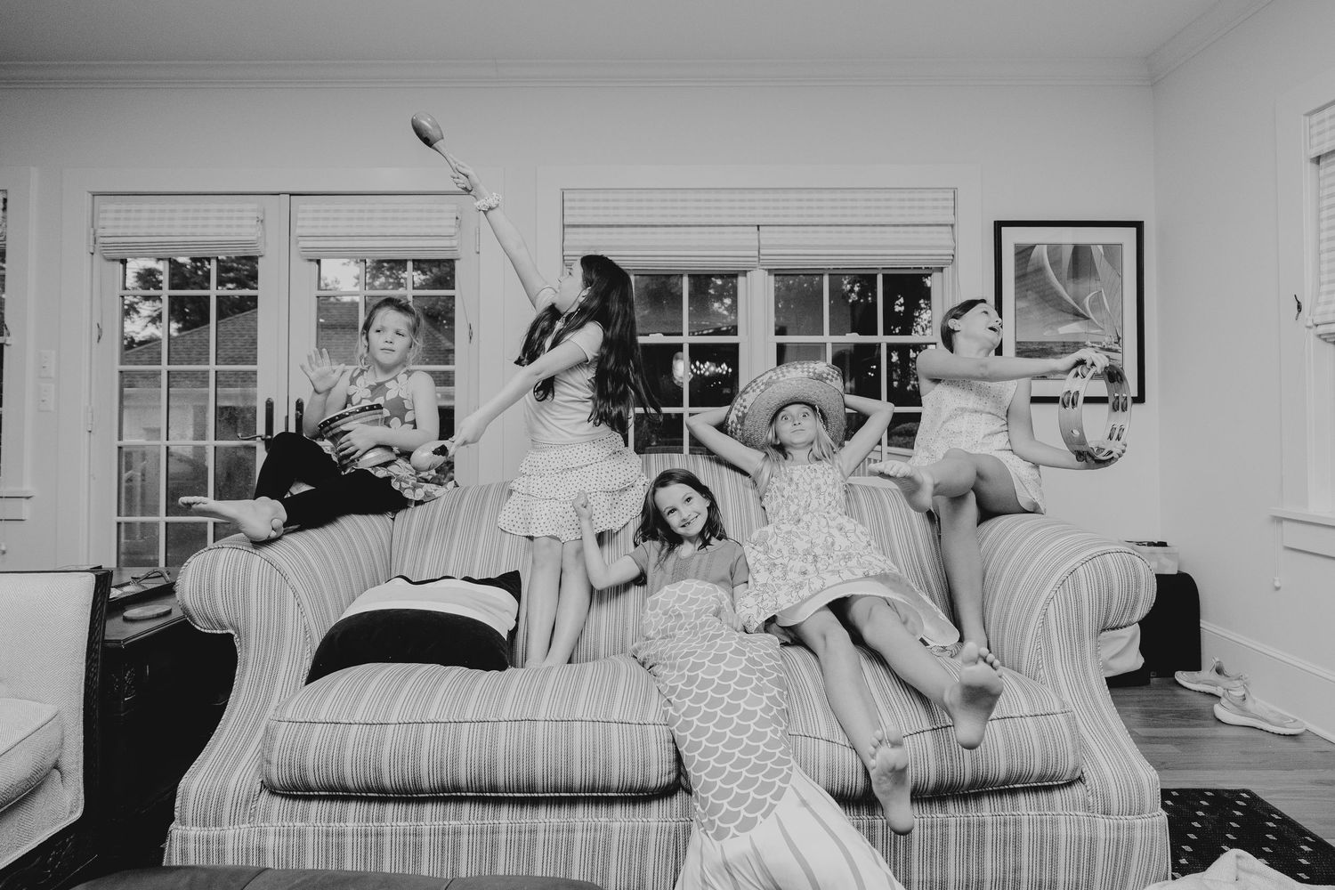Black and white photo of five people lounging and posing playfully on a striped sofa in a bright living room.