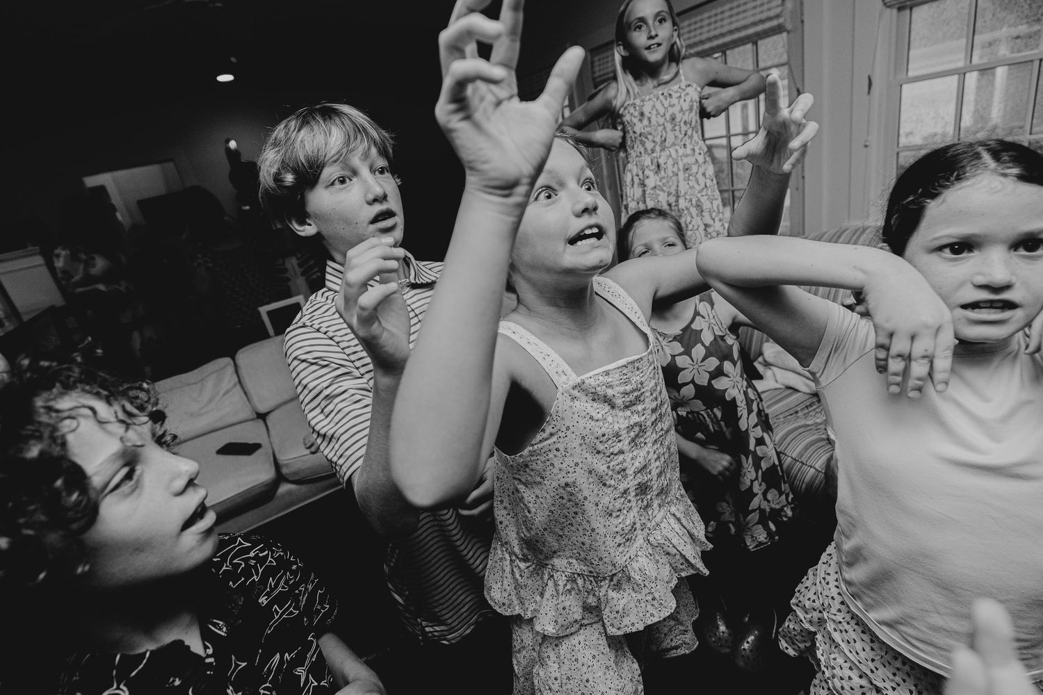 Black and white photo of children dancing and playing energetically at an indoor party or celebration.