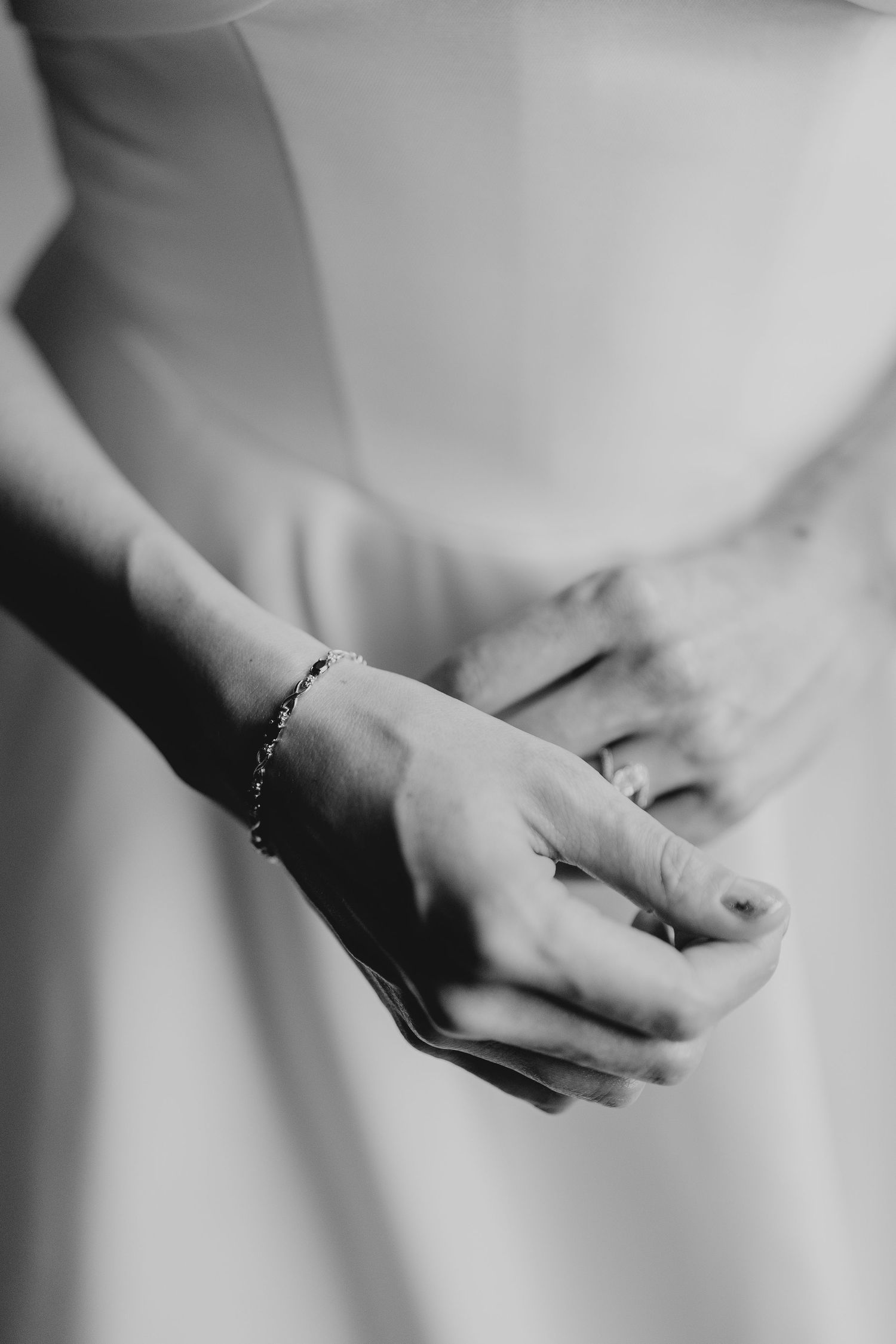 Bride's hands adjusting jewelry details against white dress.