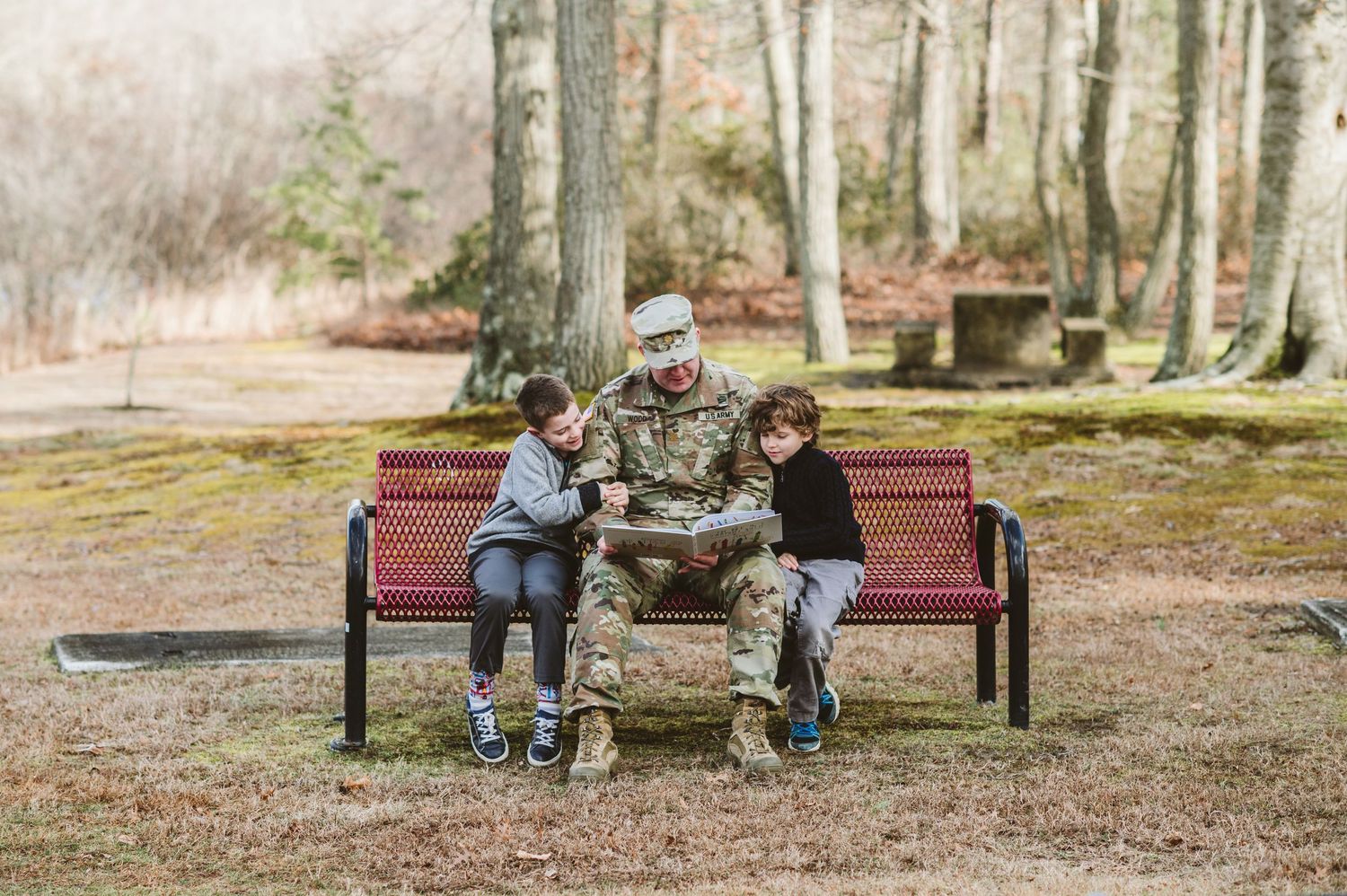 Three people sitting together on a red park bench surrounded by trees on a misty autumn day.
