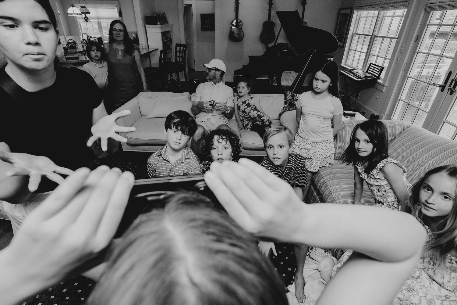 Black and white photo of a group of children gathered in a living room with a piano and guitars in the background.