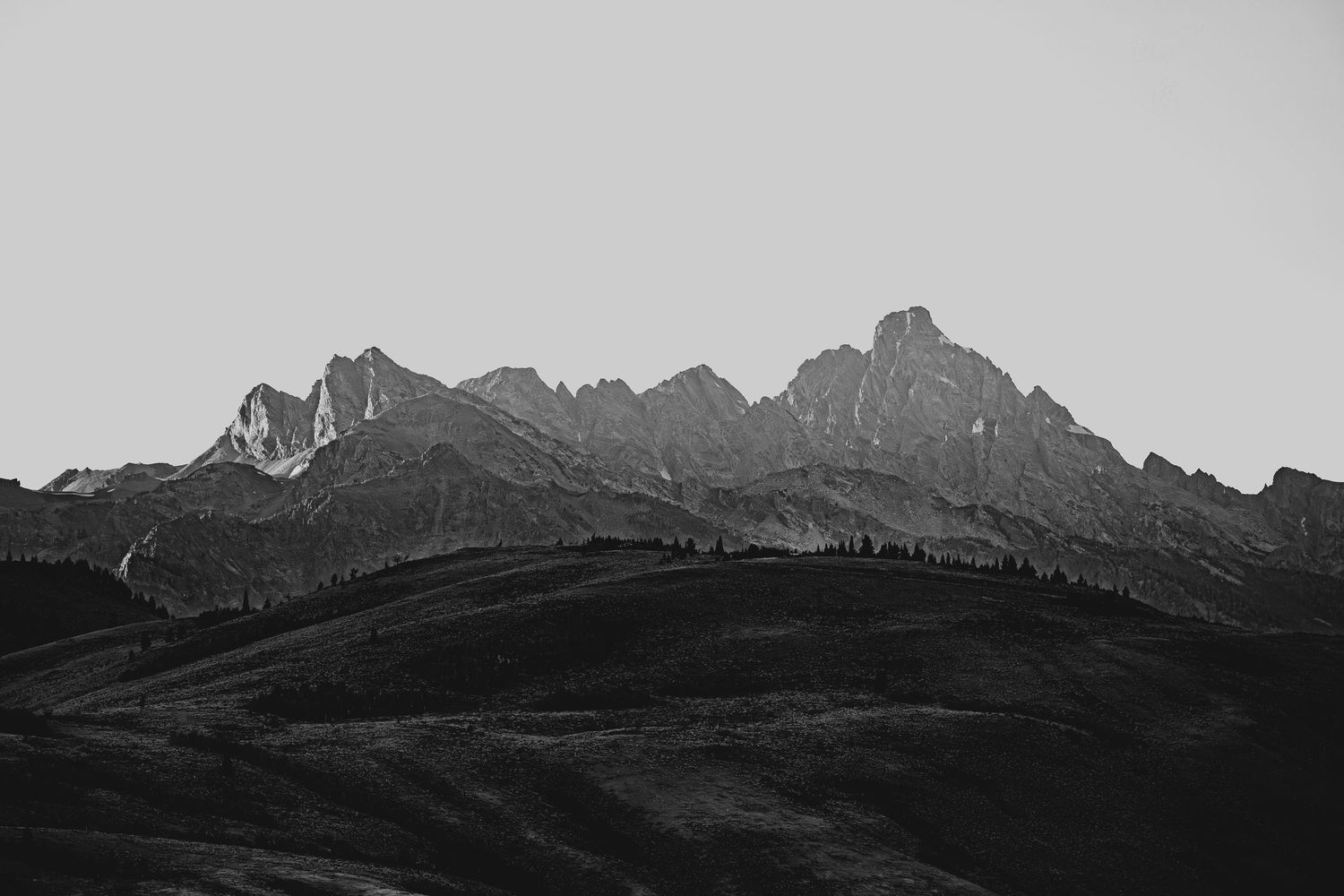 Silhouette of jagged mountain peaks against a light gray sky in a dramatic black and white landscape.