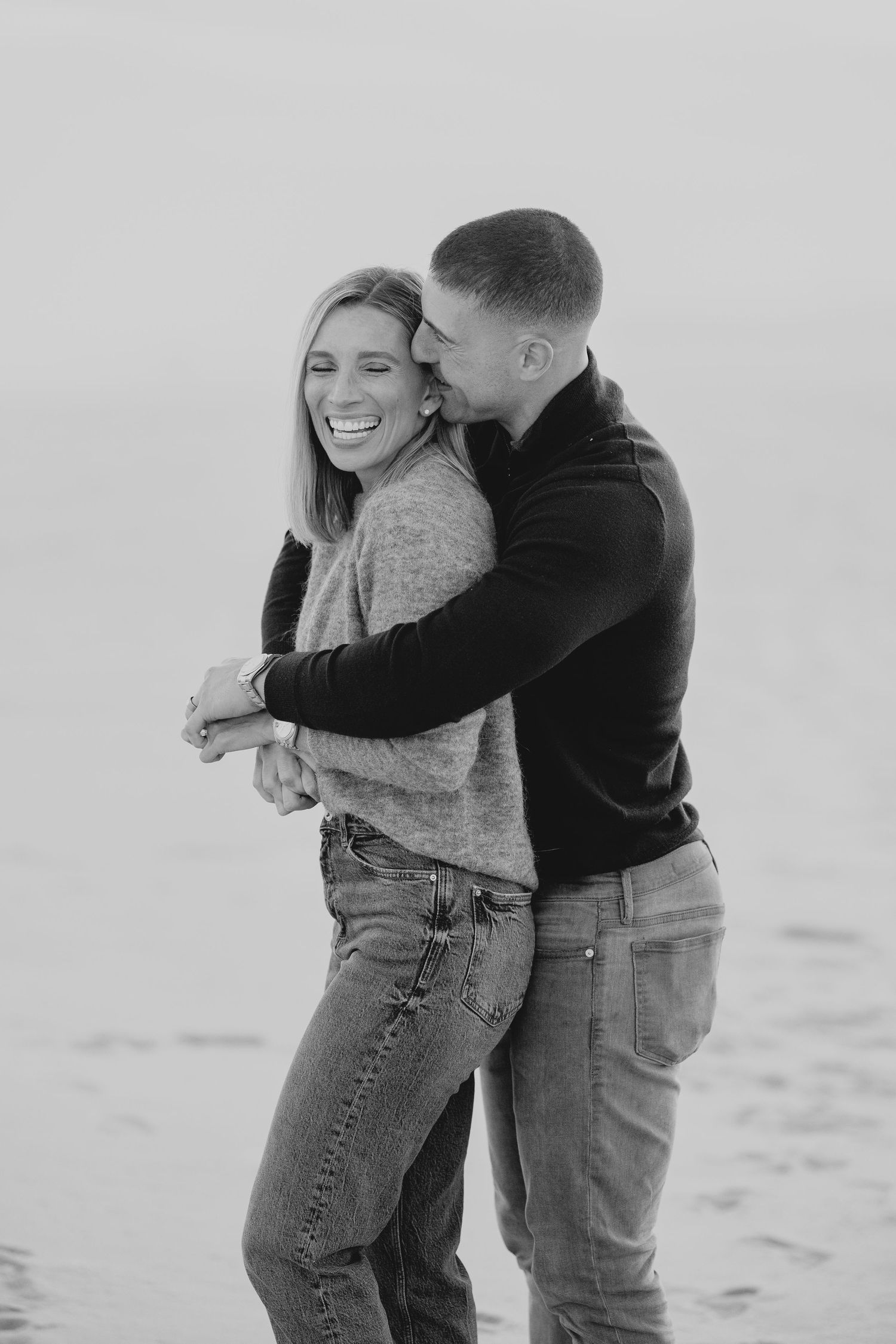 A couple laughs and embraces while enjoying a romantic moment together in black and white photography.