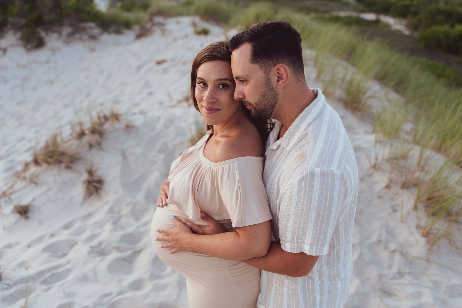 A couple shares an intimate embrace on white sand dunes near the ocean.