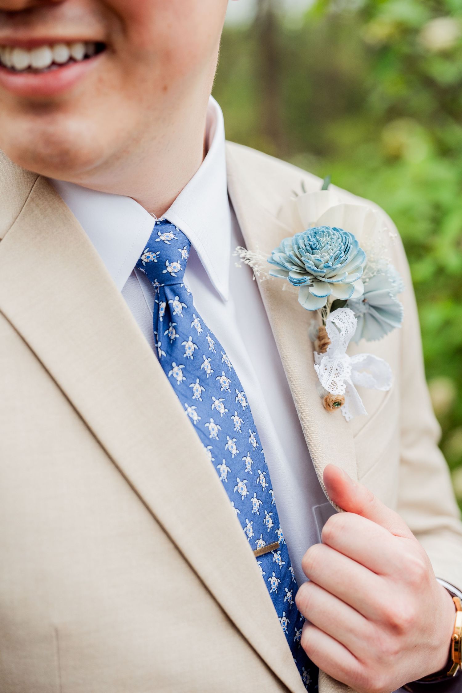 Close-up of blue patterned tie and floral boutonniere on tan suit jacket.