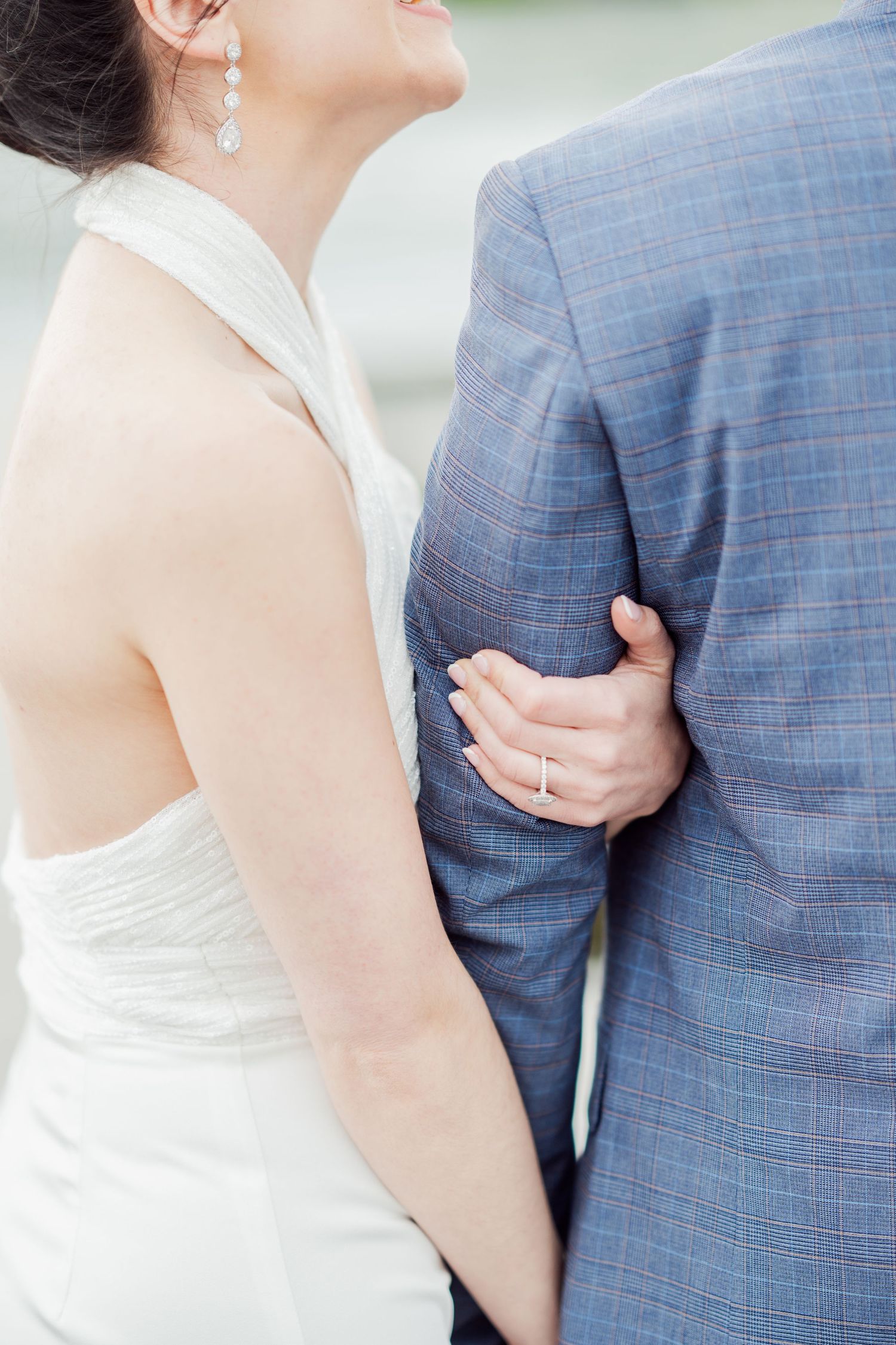 A couple in wedding attire embraces, with the bride in white and groom in a blue checkered suit.