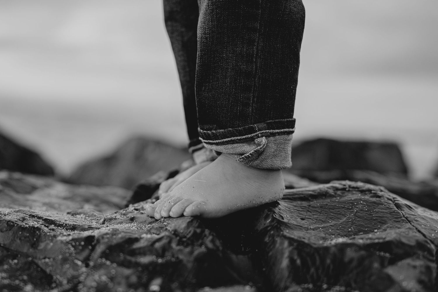 Close-up black and white photo of a child's bare feet standing on rocky surface.