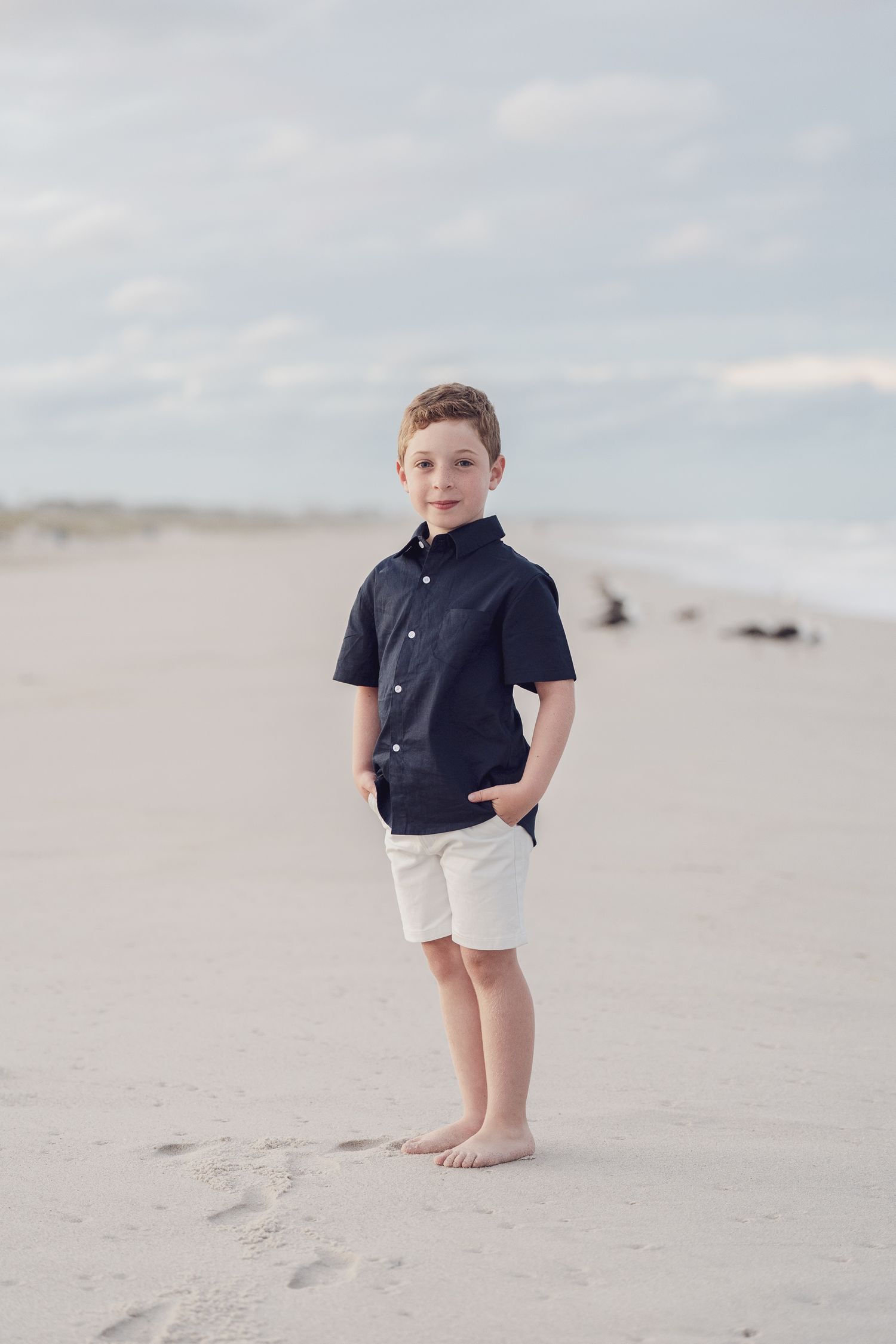 Young person in navy shirt and white shorts standing on sandy beach.