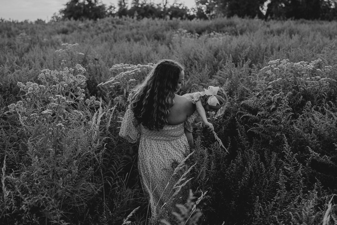 People walking through tall grass and wildflowers in a meadow.