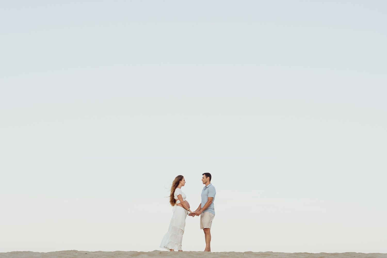 Wide landscape shot of couple on empty beach with soft lighting.