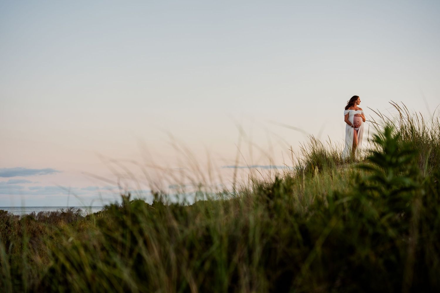 Silhouette of person standing on grassy dune during sunset.