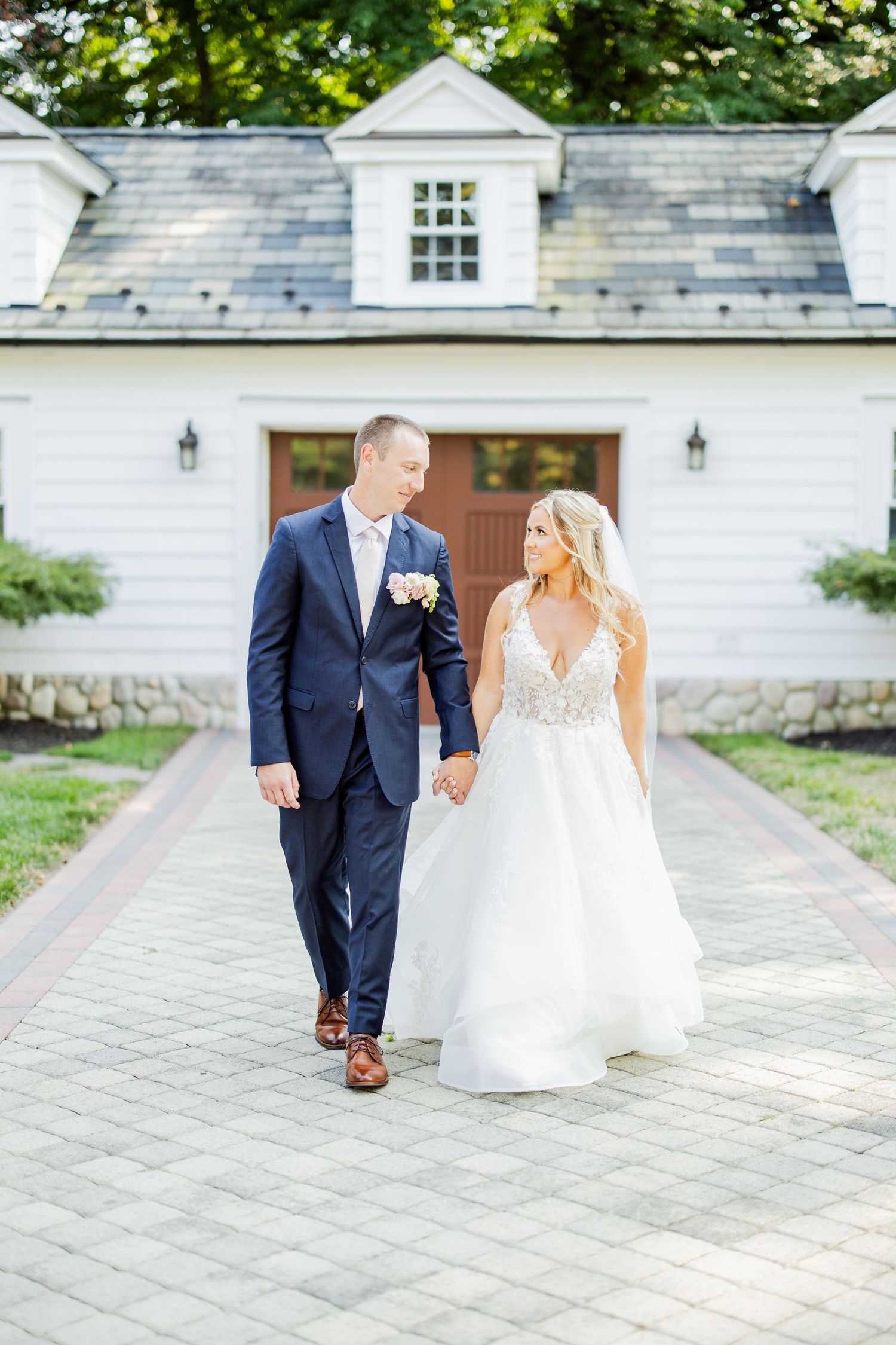 Newlyweds walking together on stone path in front of white colonial style building.