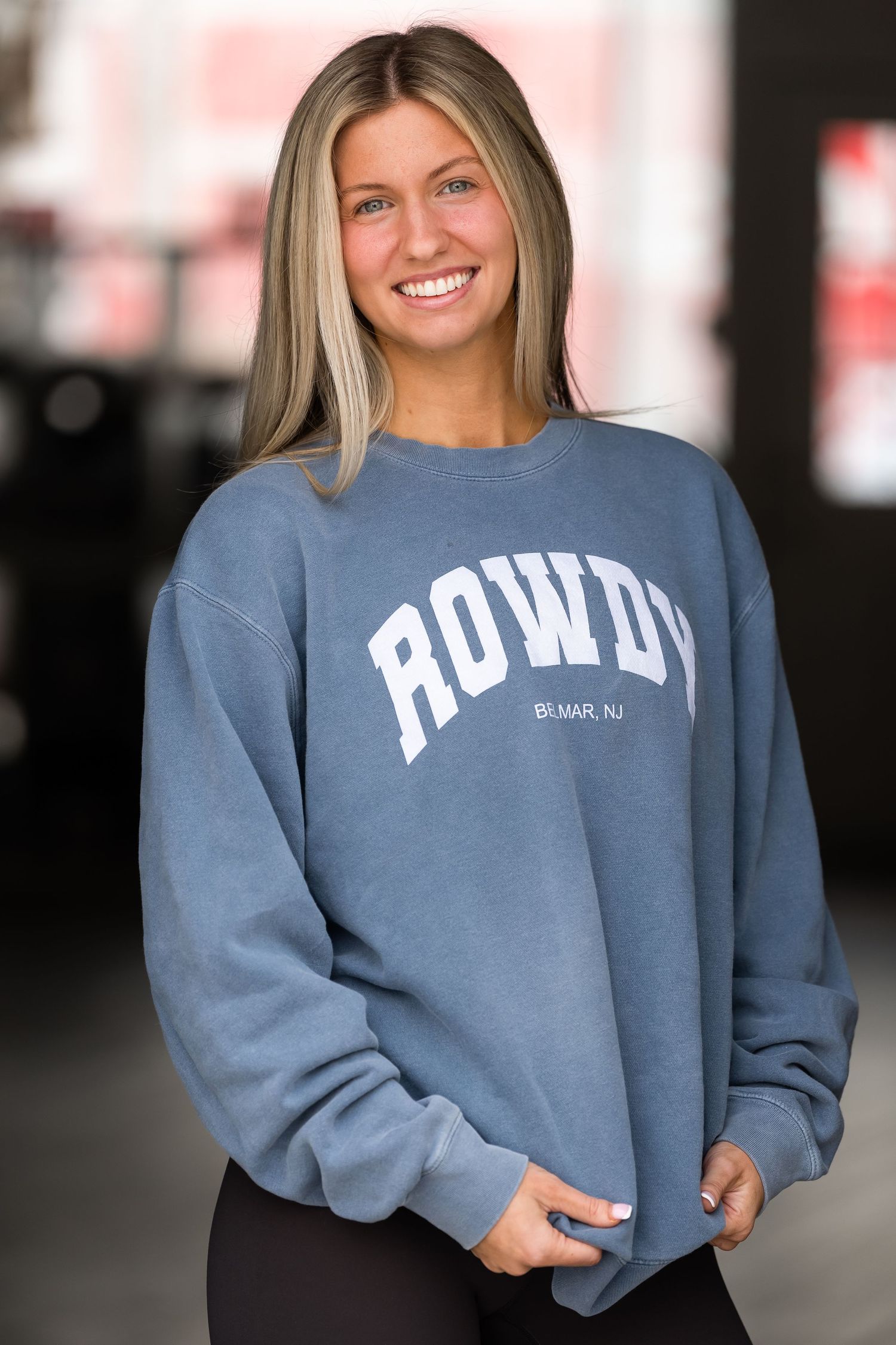 Woman smiling in a blue ROWDY crewneck sweatshirt paired with black leggings.