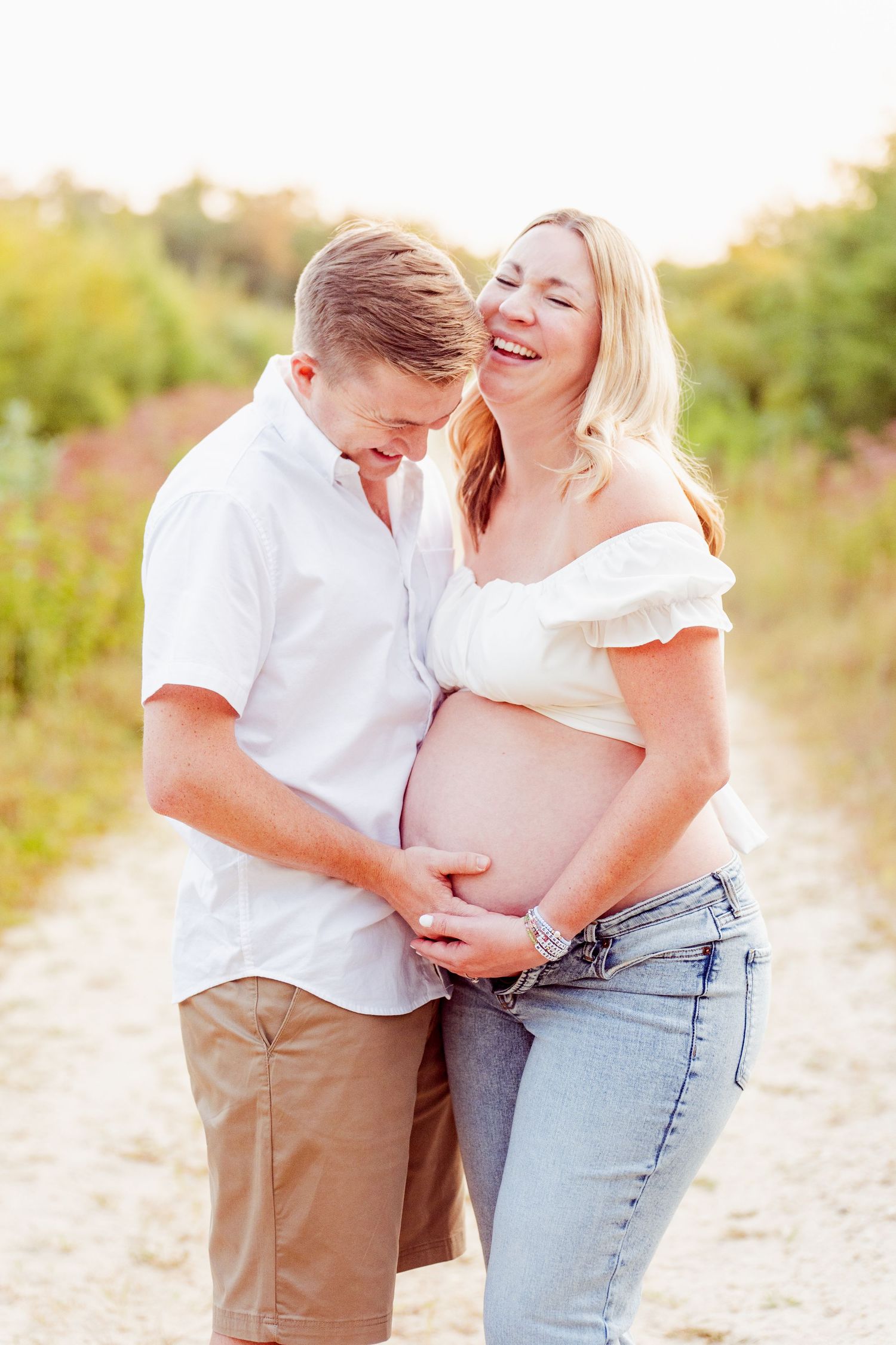 Romantic couple embraces on a sunny beach during maternity photoshoot.