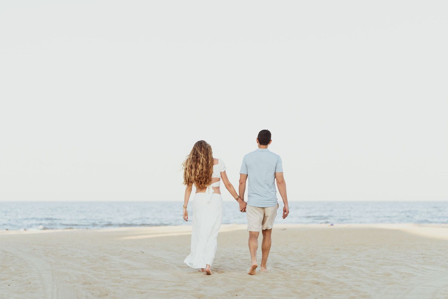 Distant view of couple walking along empty beach shoreline at sunset.