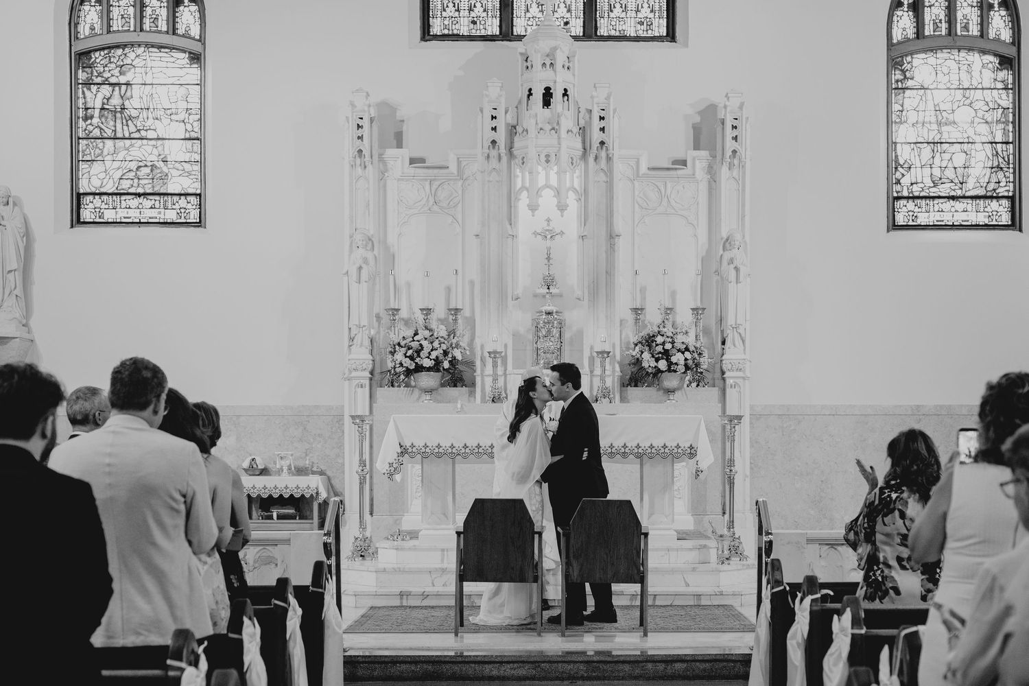 Black and white photo of a couple kissing at the altar during a church wedding ceremony with guests seated in pews.