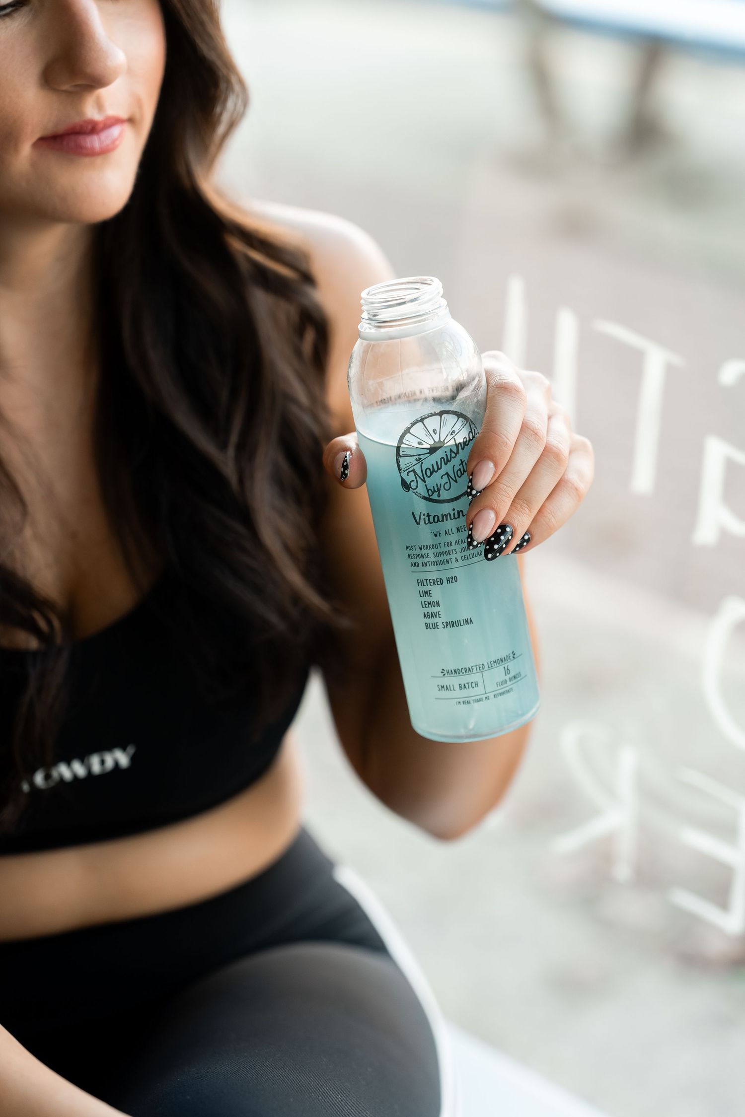 A person in black activewear holds a blue glass water bottle against a bright background.