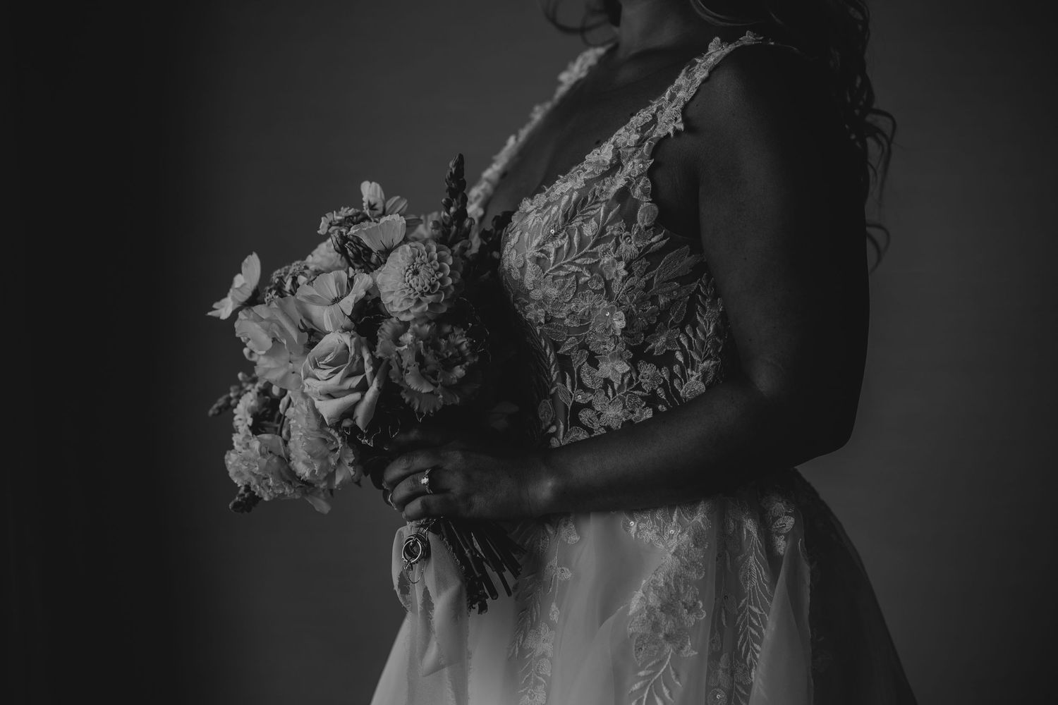 Dramatic low-key portrait showcasing intricate lace details of wedding dress bodice.