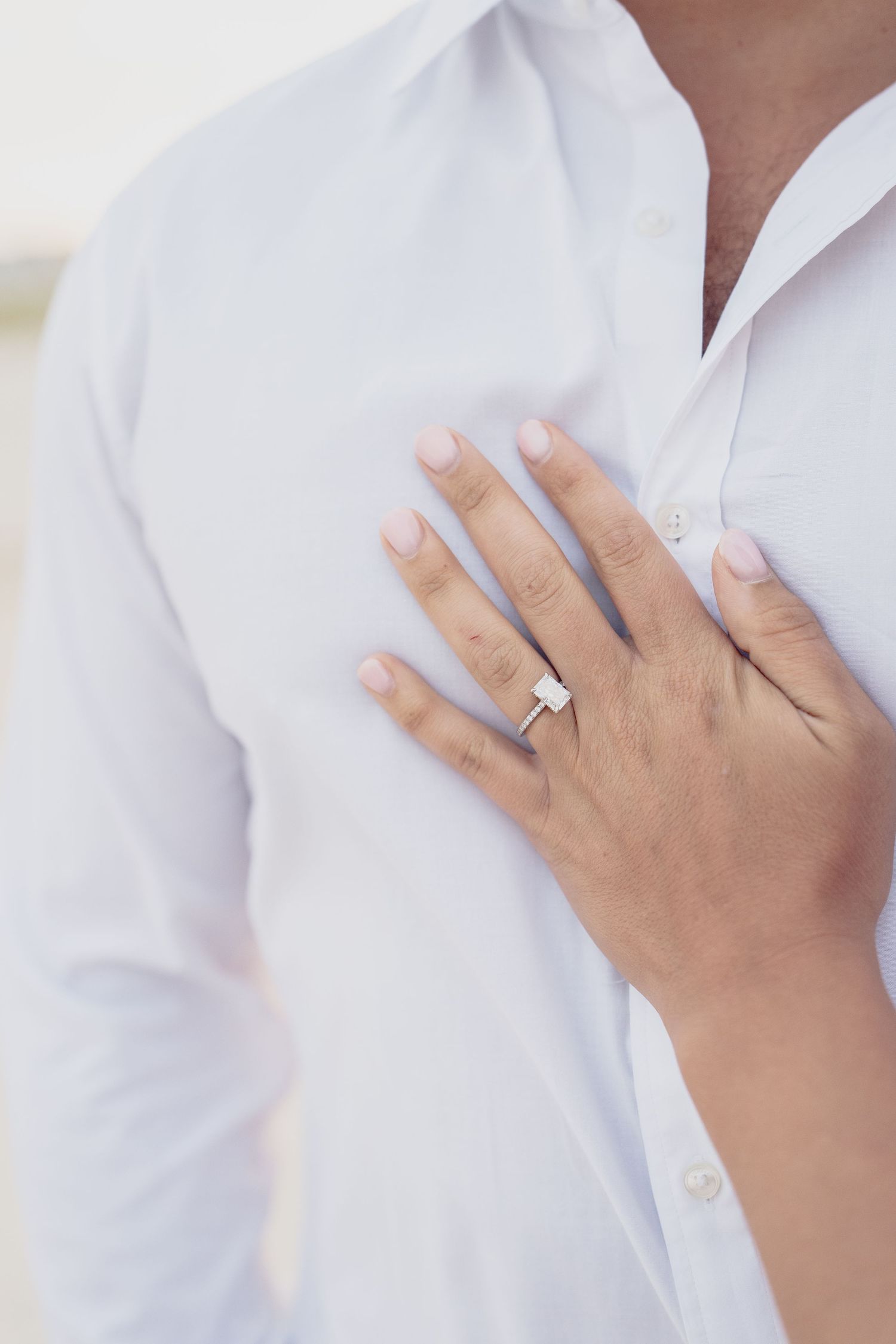 Close-up shots of hands wearing an engagement ring against a white shirt.