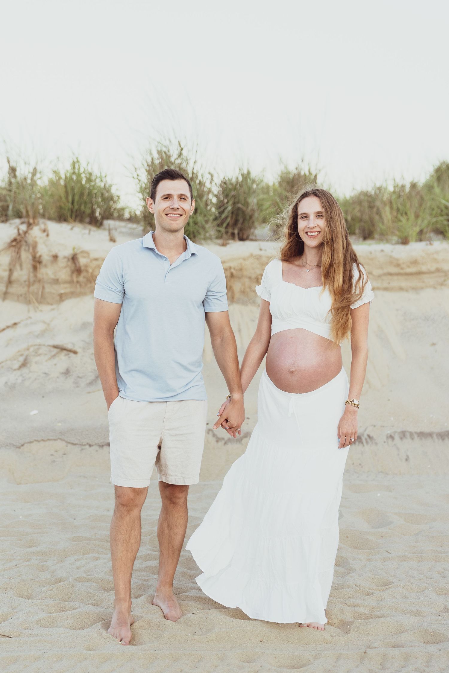 A couple walking barefoot together on a sandy beach at sunset.