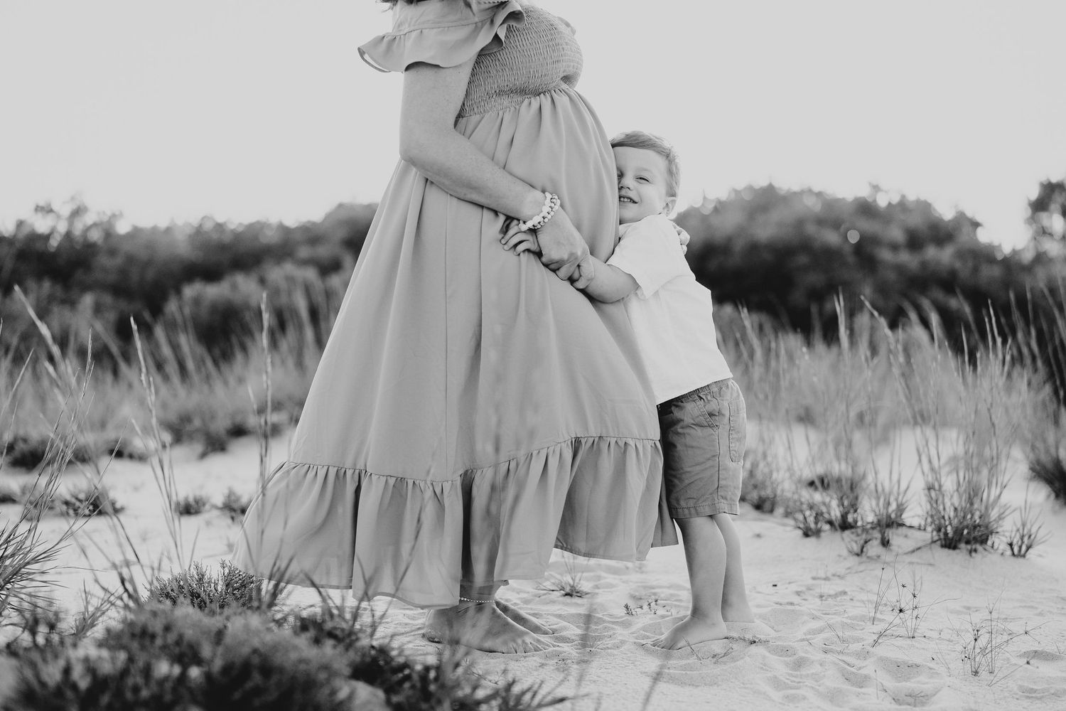 A couple shares an intimate moment while standing in tall grass near the ocean.