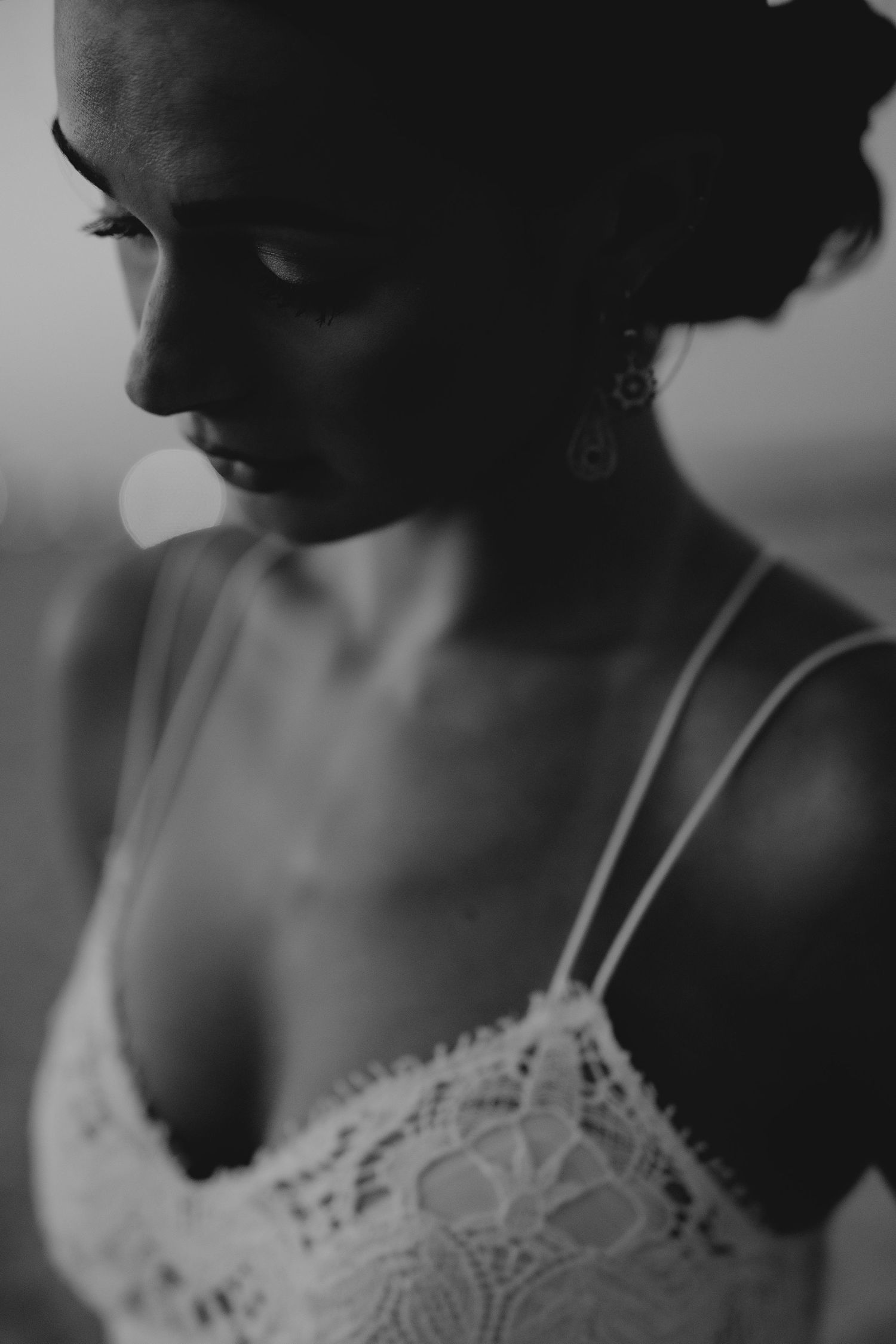Black and white portrait of a bride in lace camisole dress with elegant earrings, looking down gracefully.