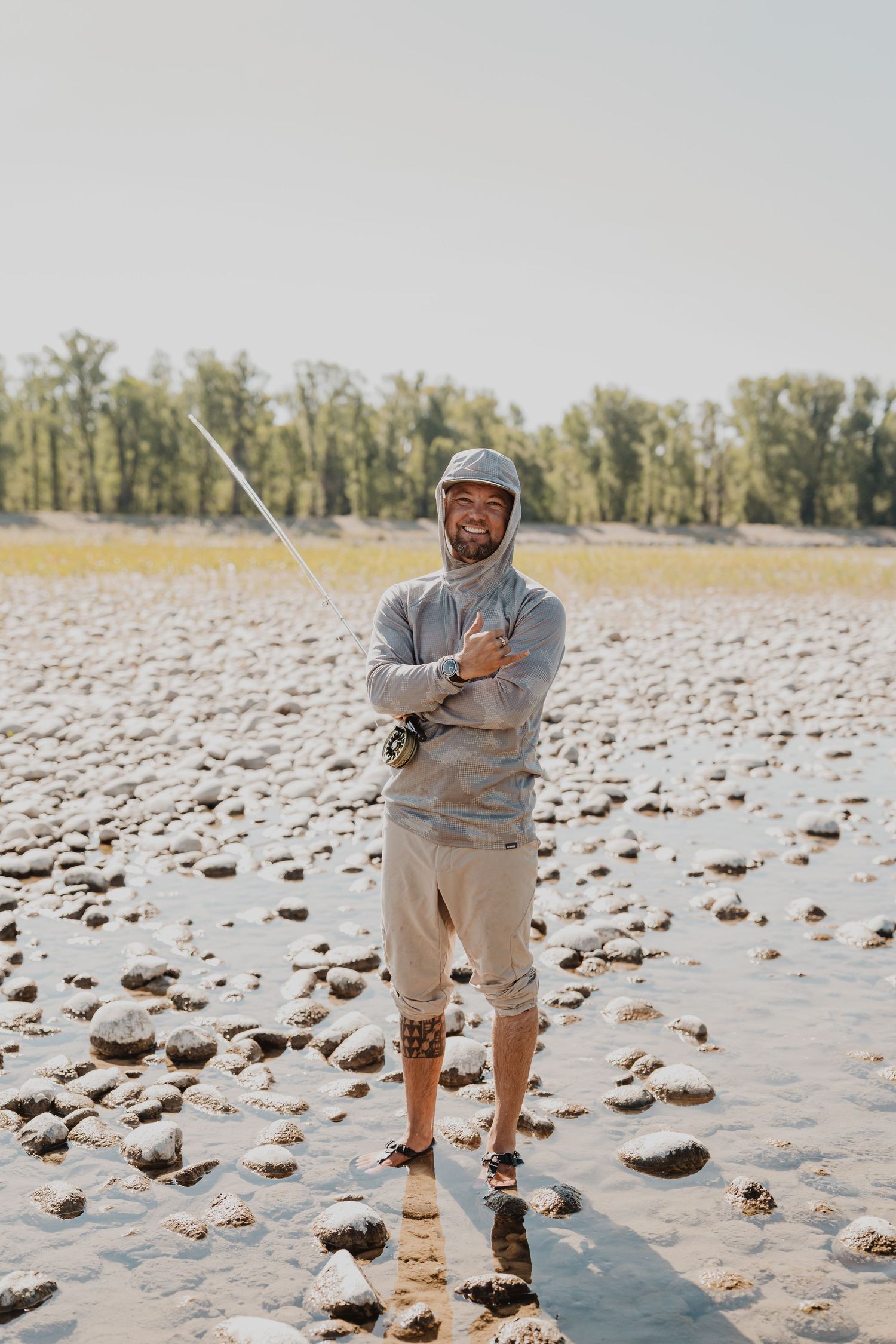 A person in casual attire stands on a rocky beach, making playful poses in a sequence of four connected photos.