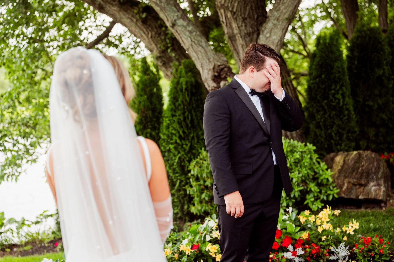Elegant wedding portraits captured under large trees with red flowers blooming nearby.