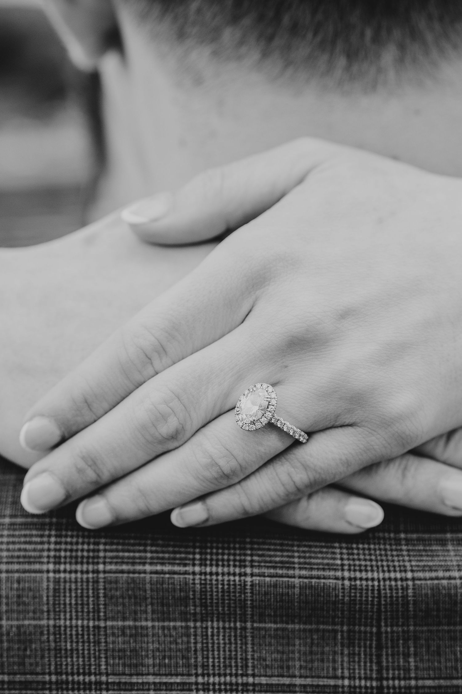 Black and white detail shot of hands with engagement ring resting on textured fabric.