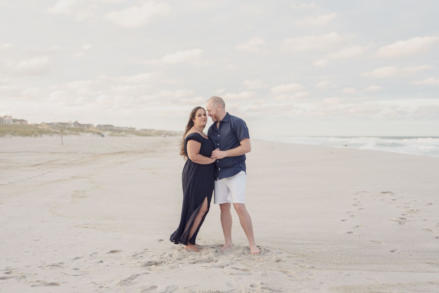 Couple in casual attire sharing intimate moments during beach photoshoot.