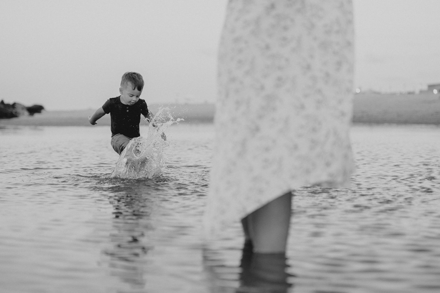Black and white photo of splashing in shallow water with a flowing dress in the foreground.
