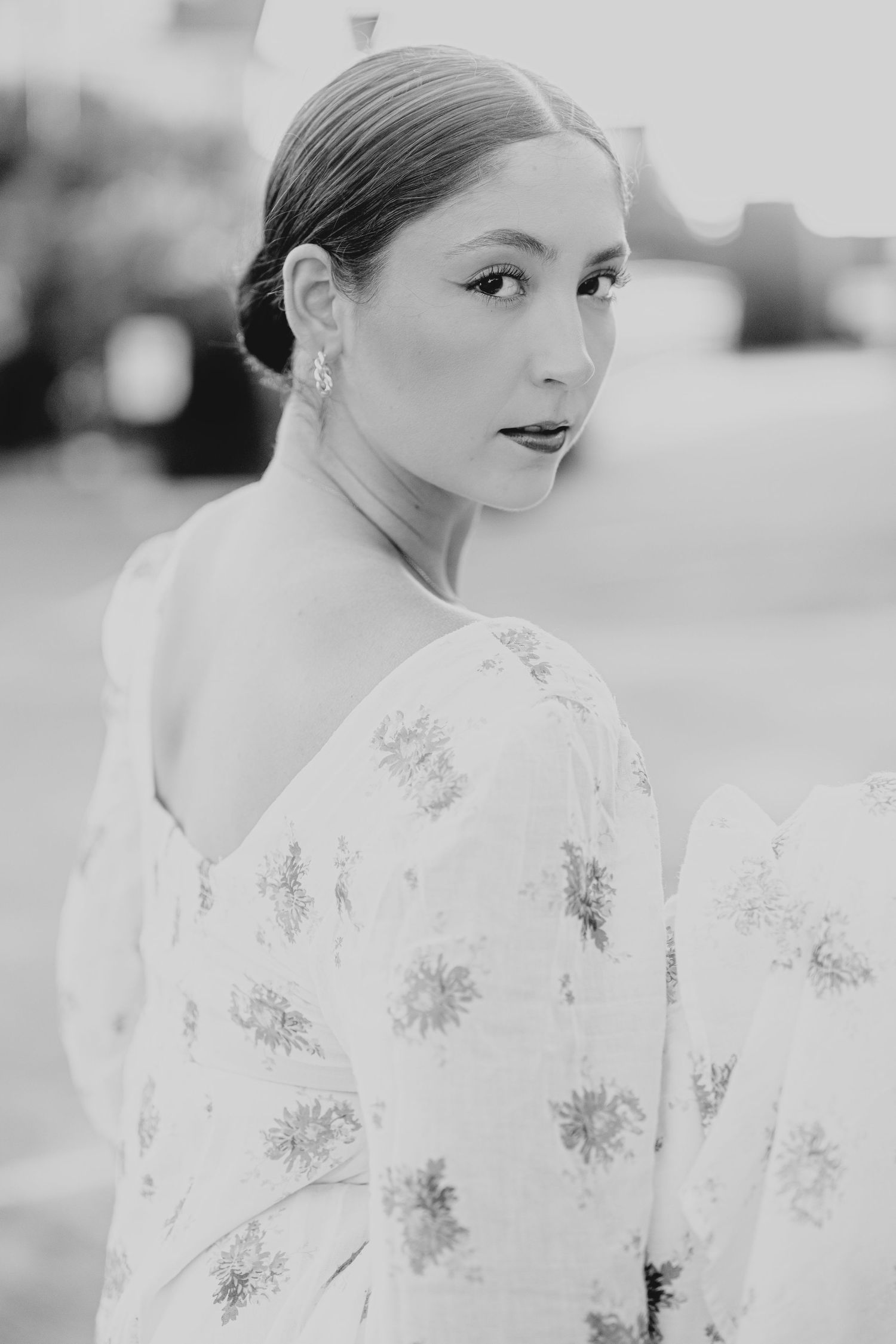 Black and white portrait of elegant woman in floral off-shoulder dress with sleek updo and drop earrings.