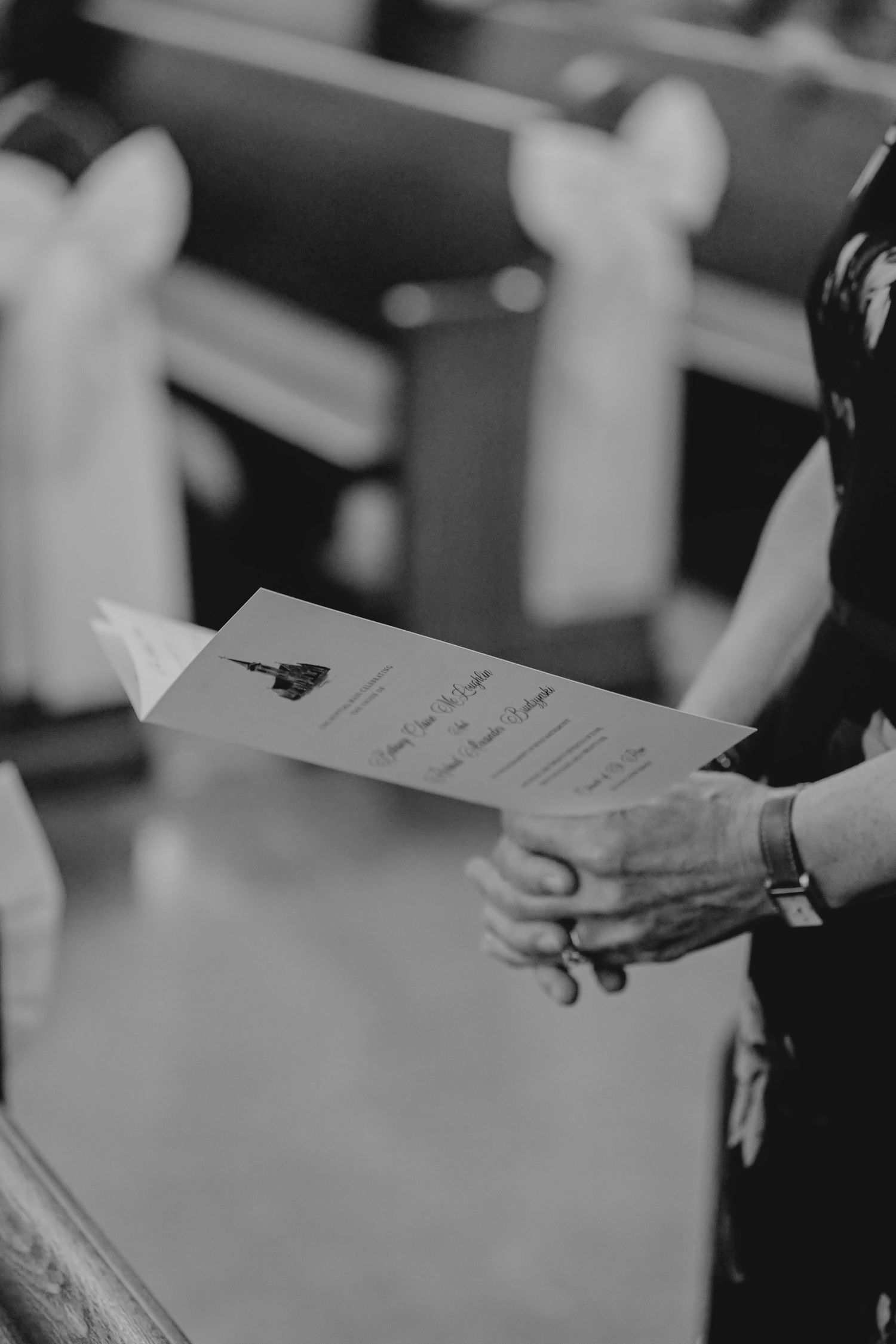 Black and white photo of hands holding a wedding ceremony program inside a church with pews in the background.