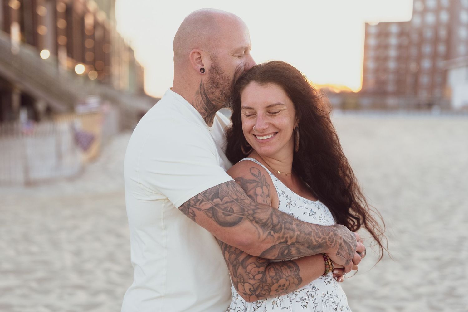 A romantic moment between a couple embracing on a sandy beach at sunset.