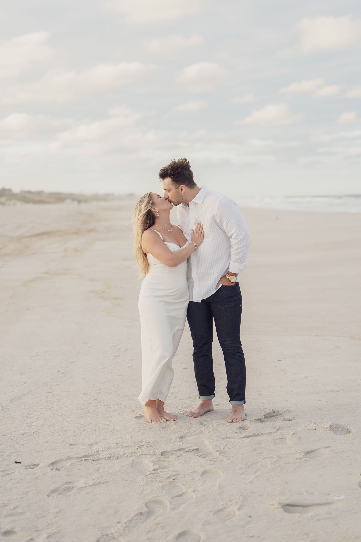 Couple sharing intimate moment on sandy beach under cloudy sky.