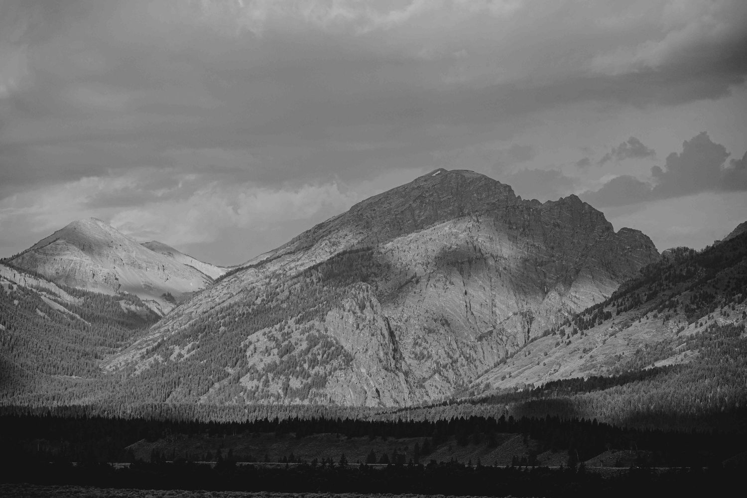 A dramatic black and white landscape of rugged mountain peaks under cloudy skies in a remote wilderness area.