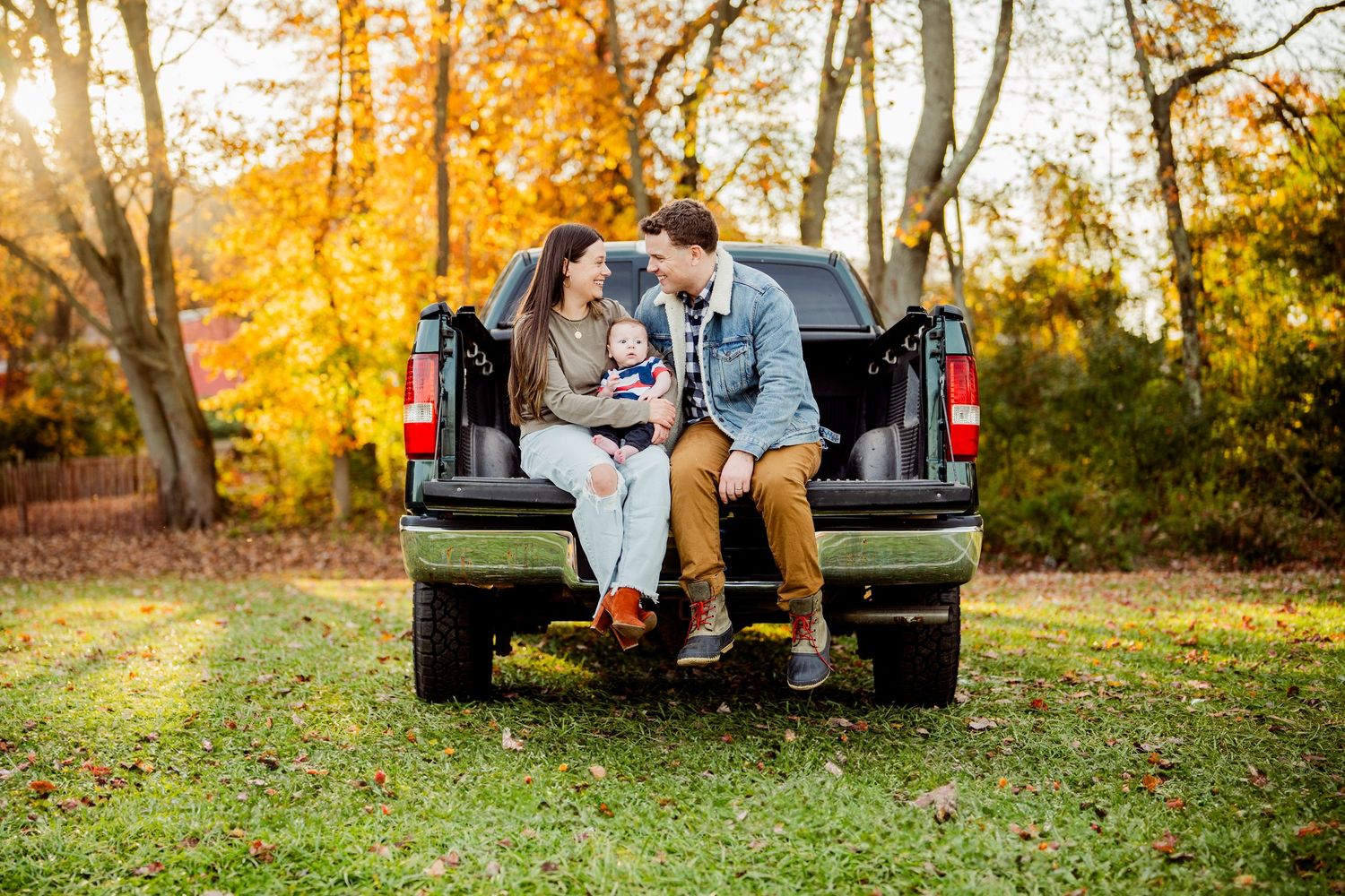 Autumn scene with couple sitting on truck tailgate surrounded by golden foliage.