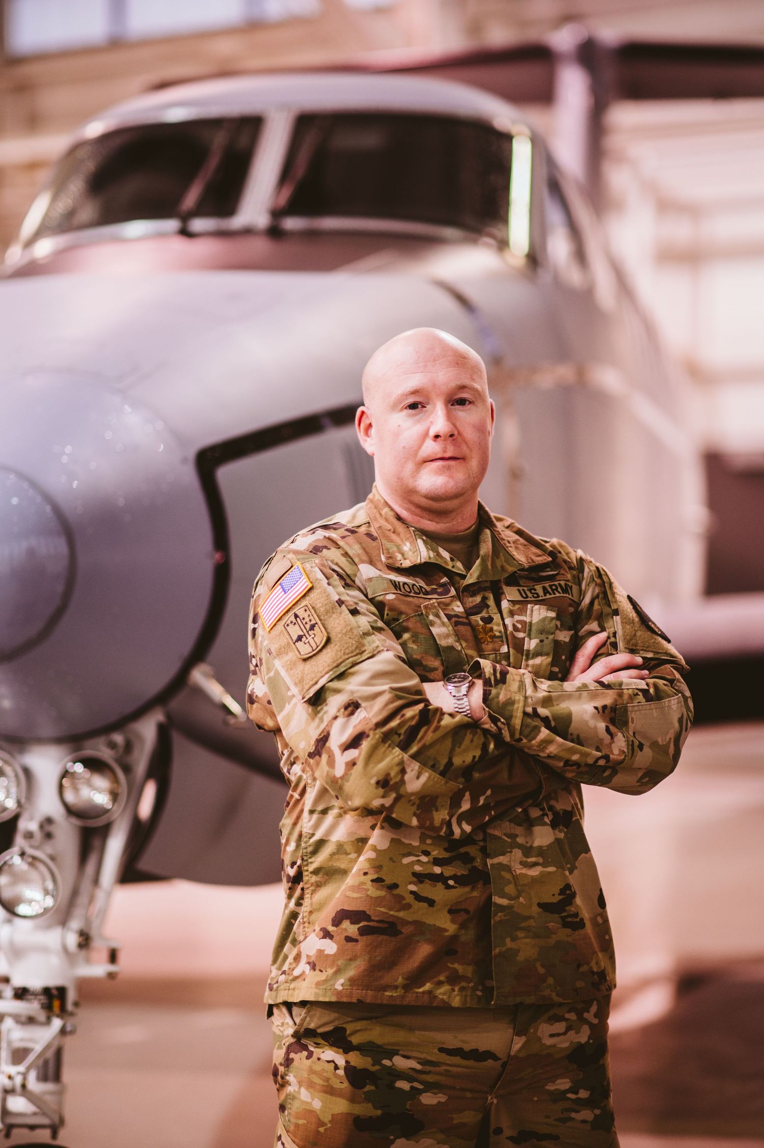 Military personnel in camouflage uniform stands near aircraft in hangar.