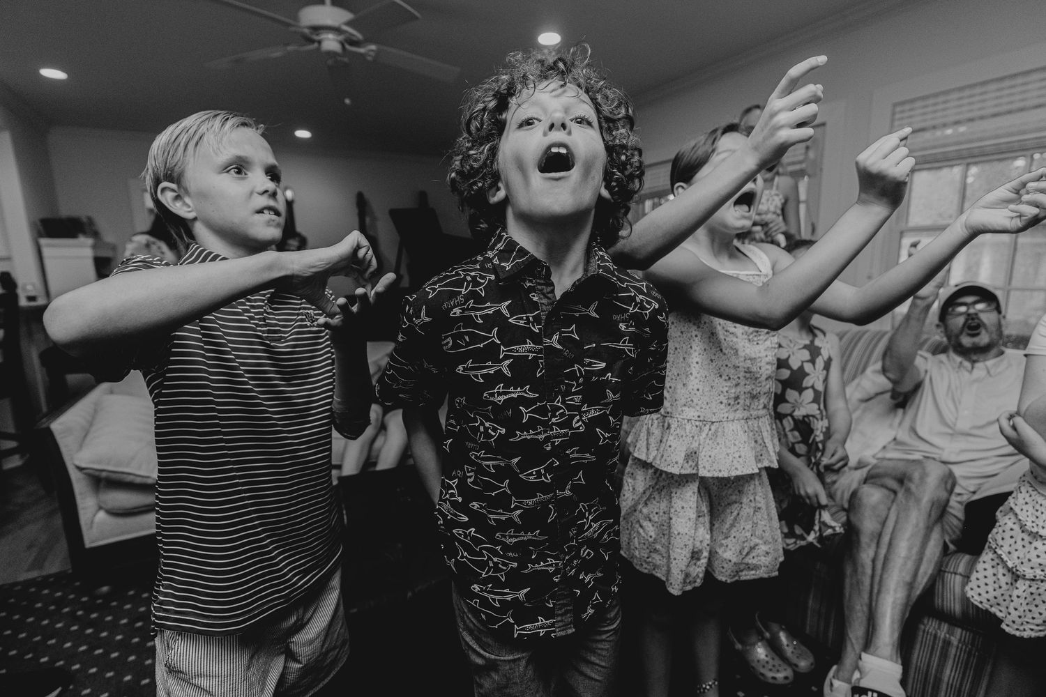 Children dancing joyfully at a party in black and white photography, arms raised with excitement.