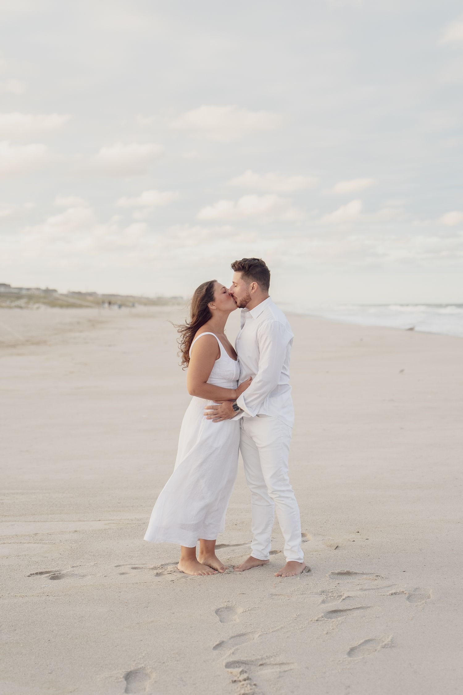 Couple in white outfits sharing romantic moments on a sandy beach.