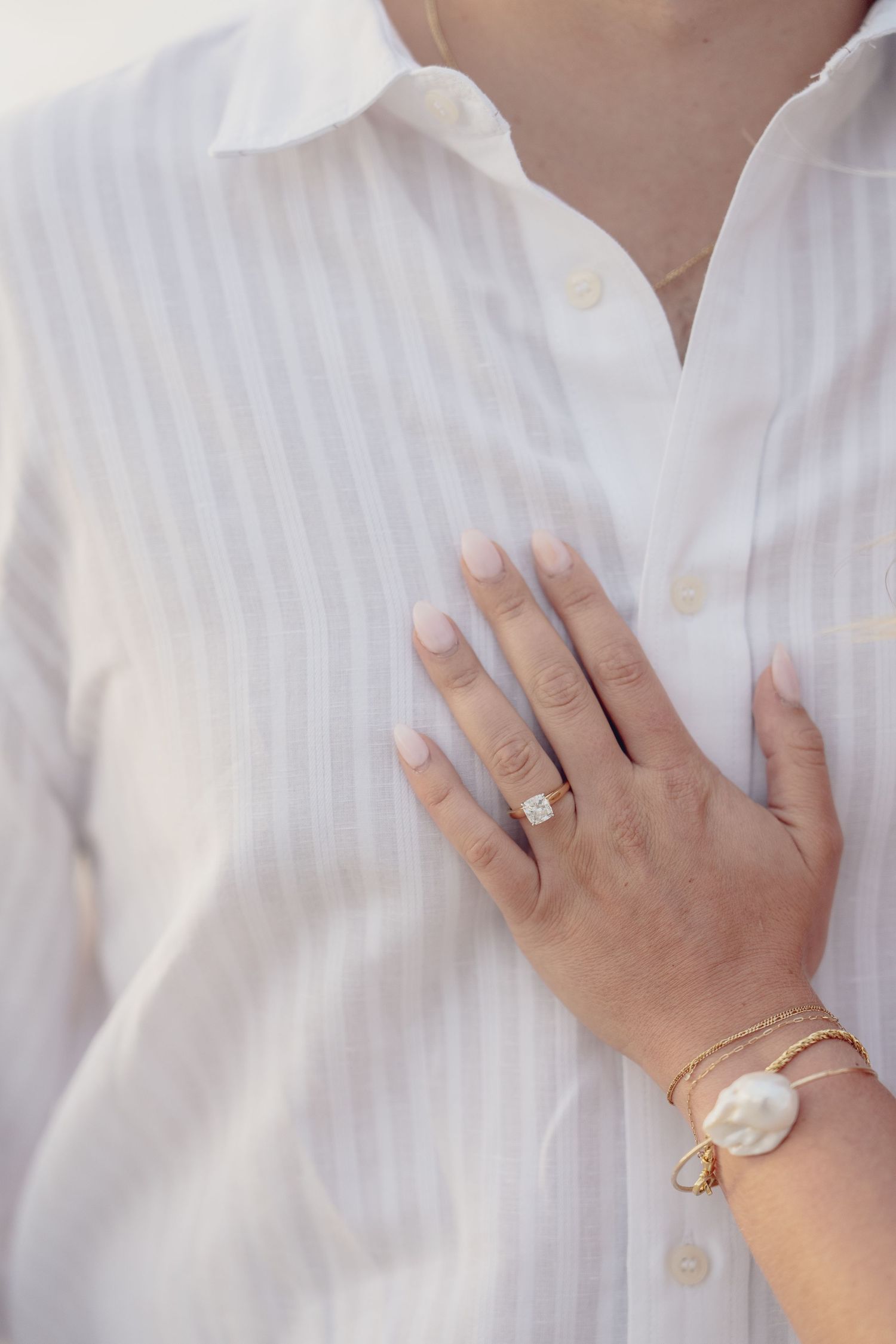 Close-up of hands wearing pearl jewelry and rings against white striped fabric.