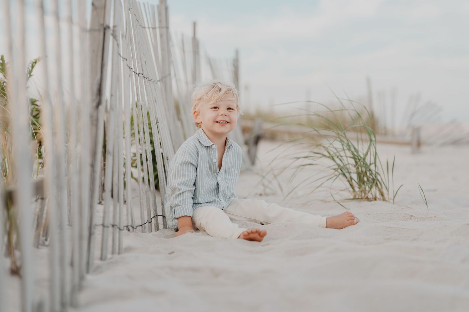 Family enjoying a playful moment together on a sandy beach with wooden fences in the background.